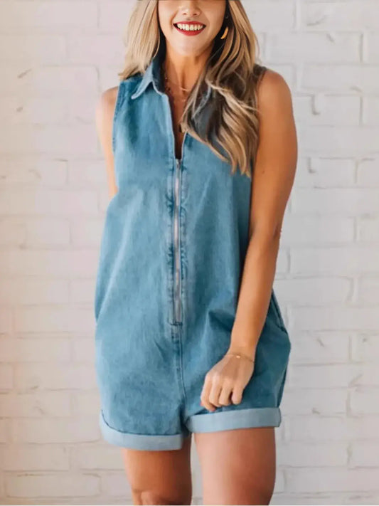 Woman wearing a zip front sleeveless denim romper against a white brick wall