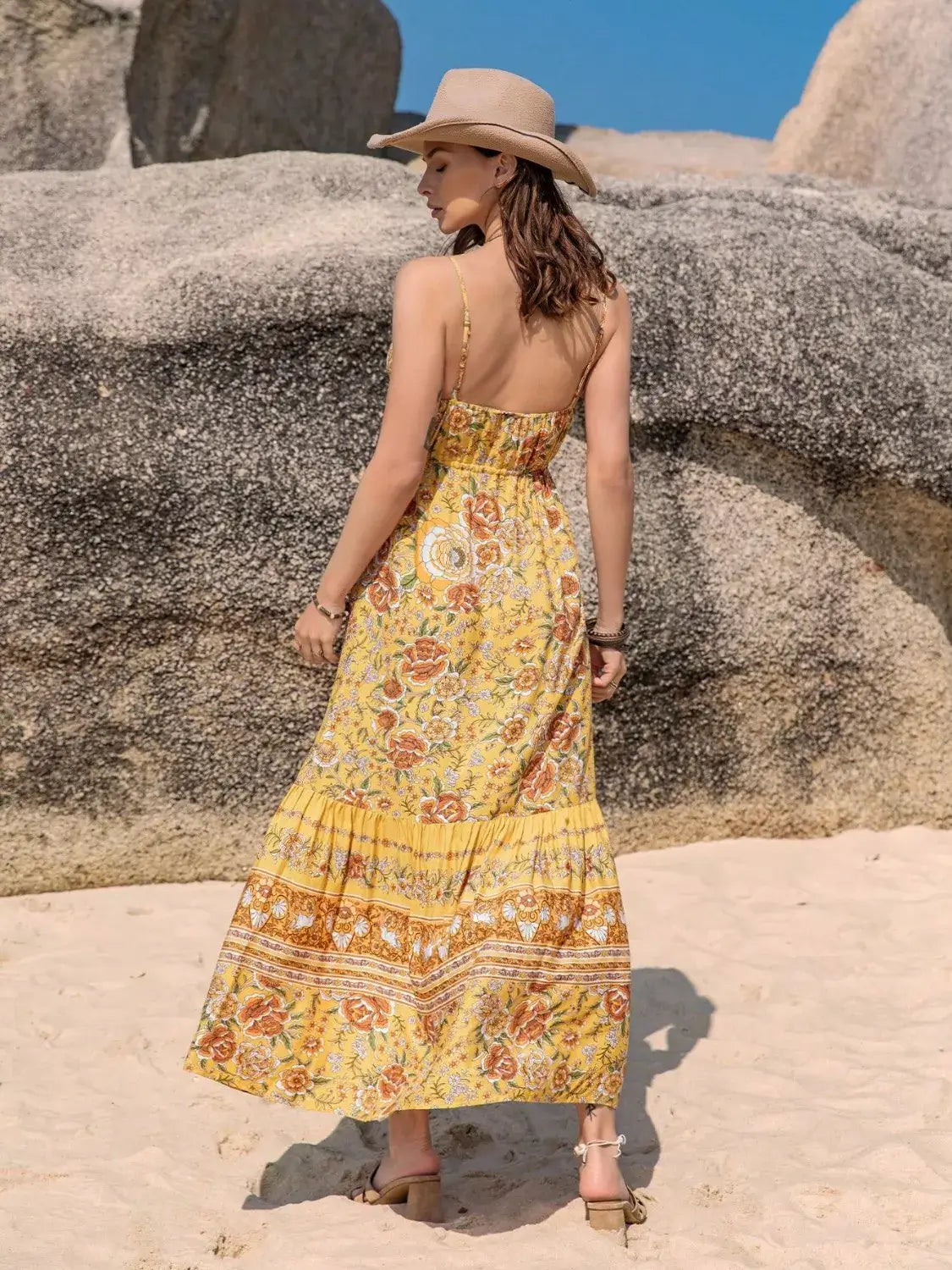 Woman in a yellow floral Tassel Printed Tiered Cami Dress, enjoying a sunny beach day with a stylish hat.