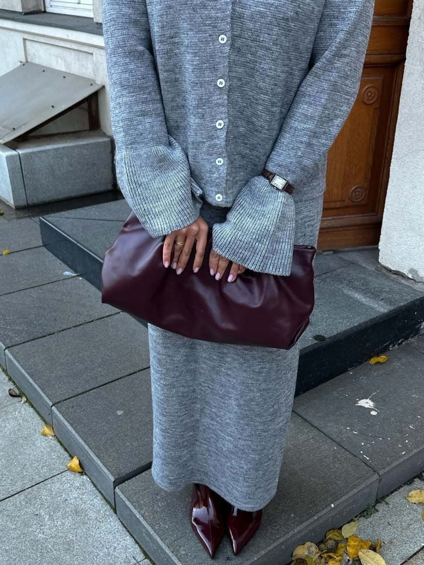 Woman wearing a Button Down Cardigan and Skirt Knit Set, holding a burgundy handbag, standing on outdoor steps.