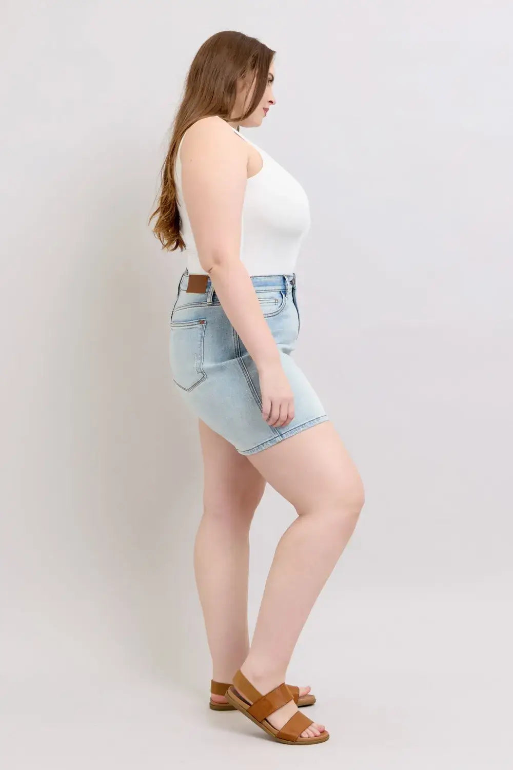 Plus size woman modeling Judy Blue denim shorts with 2-button closure and pockets, styled with a tank top and sandals.