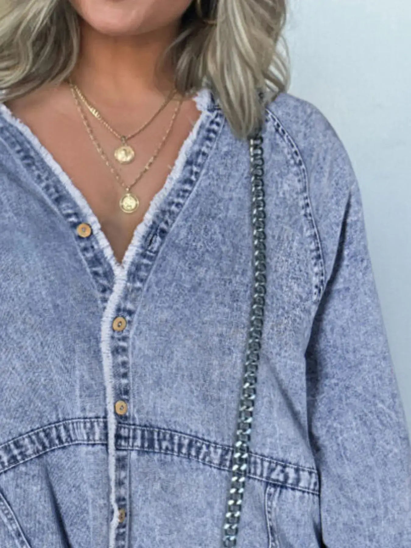Close-up of a woman wearing a button-front denim shirt dress with layered necklaces, showcasing a casual yet stylish look.