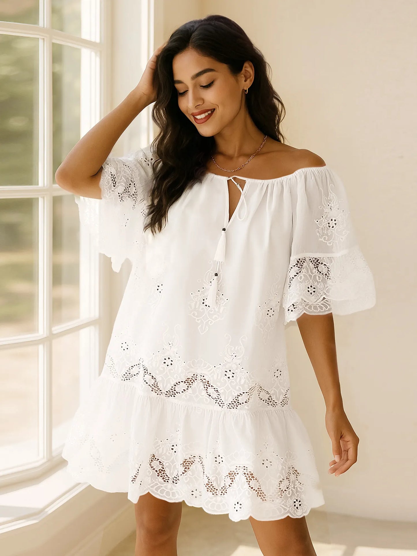 Model wearing Eyelet Embroidered Tassel Tie Neck Dress with flutter sleeves and ruffled hem in a bright indoor setting.