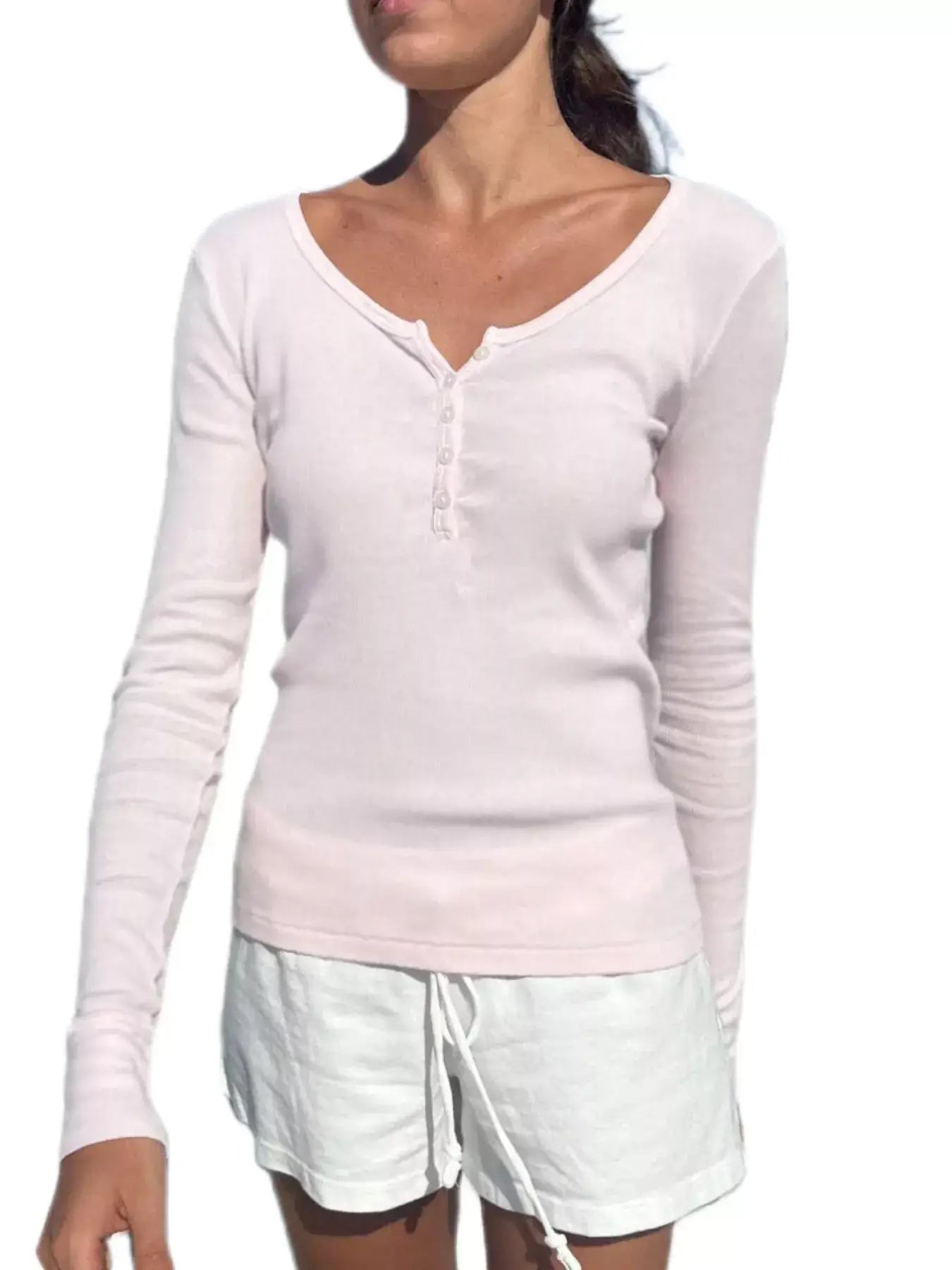 Woman wearing a light pink long sleeve Henley t-shirt with a buttoned neckline and white shorts.