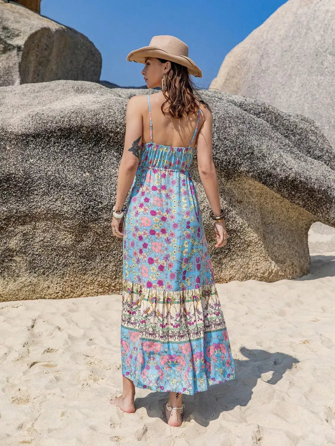 Tassel Floral Print Cami Dress showcasing back view at the beach with stones and sunlight.