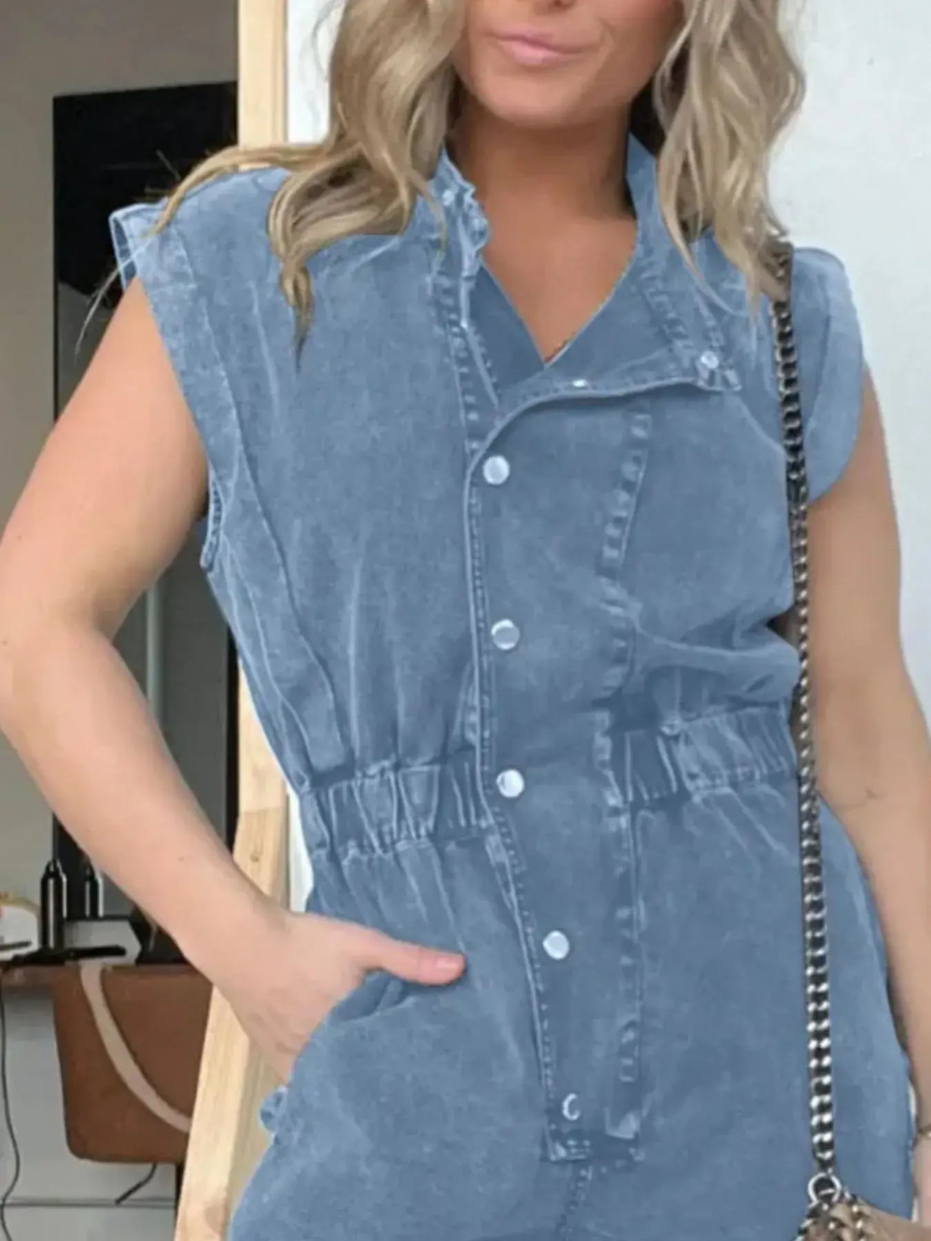 Model wearing a full size button front cap sleeve denim jumpsuit in blue, showcasing its belted waist and practical pockets.