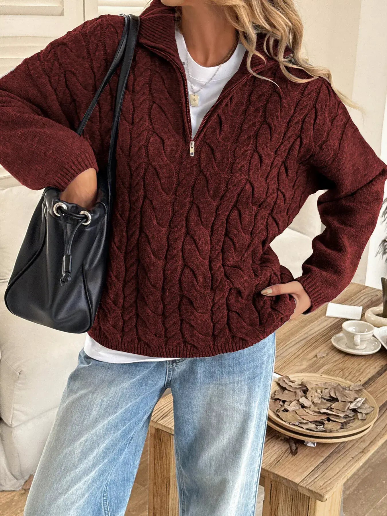 Woman wearing a zip collar cable-knit sweater in burgundy, paired with relaxed jeans and carrying a black handbag.