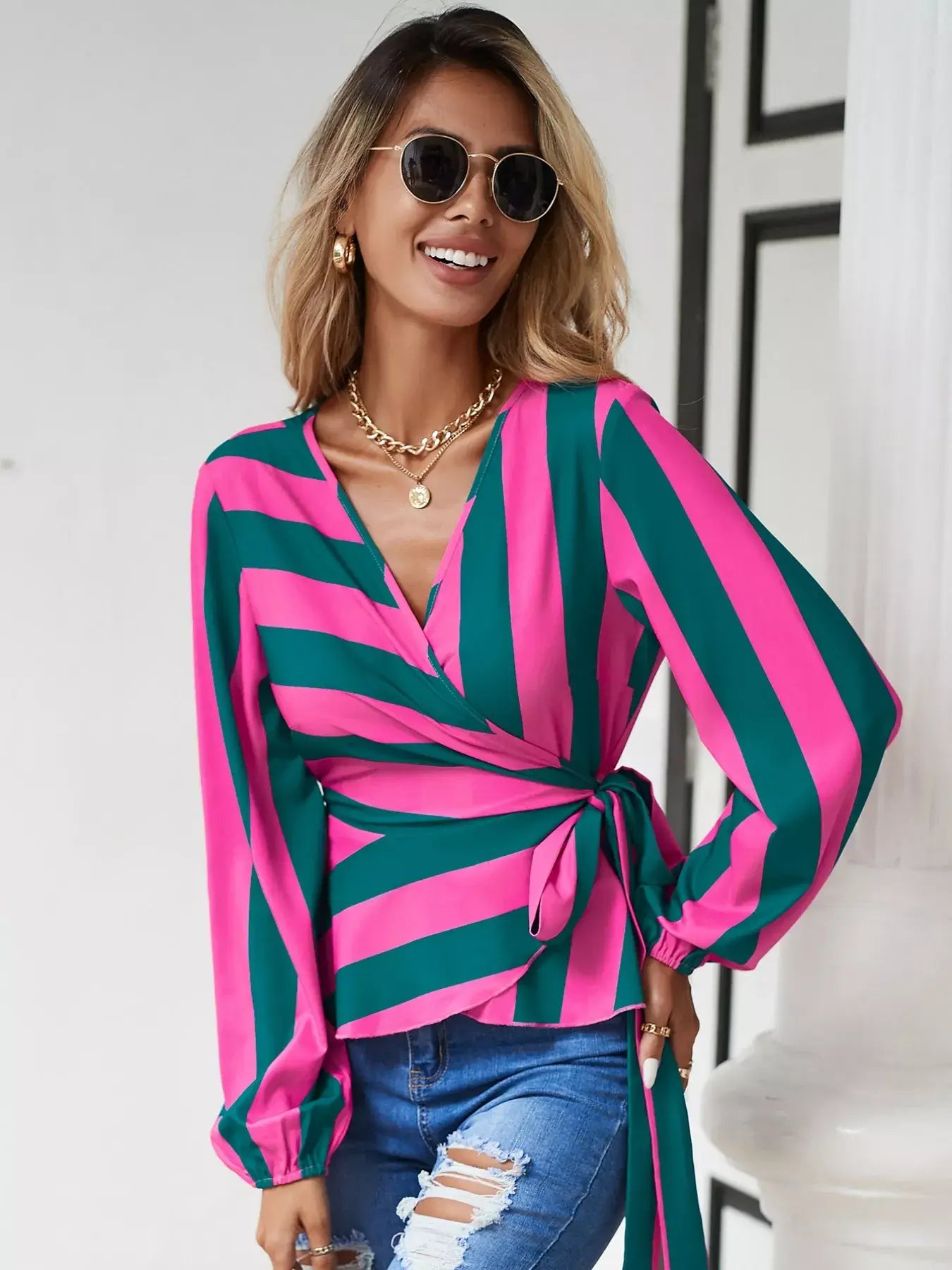 Striped wrap blouse with tie detail worn by a smiling woman, featuring pink and green stripes and stylish sunglasses.