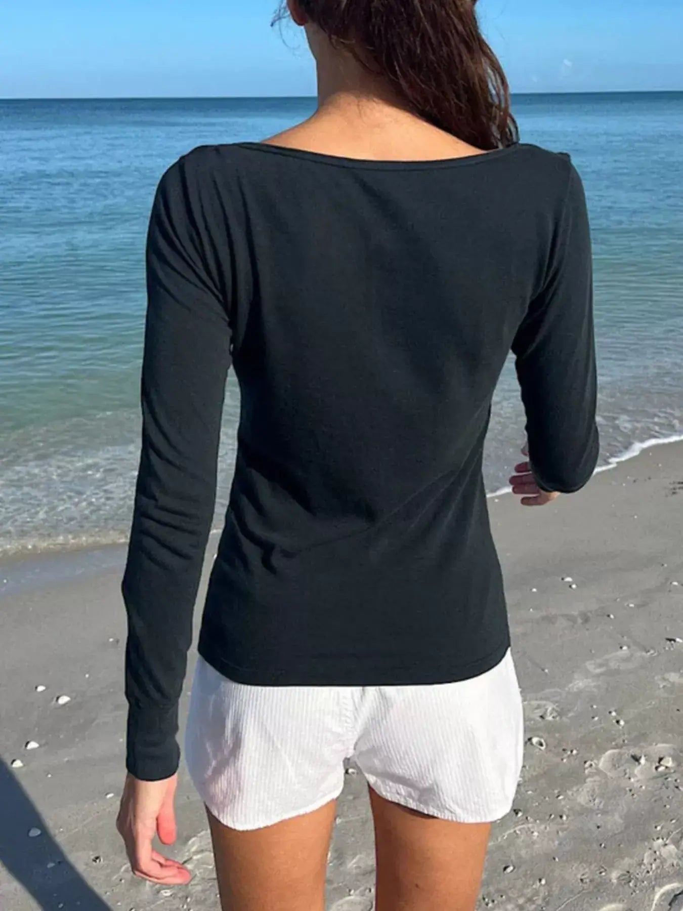 Model wearing a black long sleeve henley shirt on the beach, showcasing a casual and stylish back view.