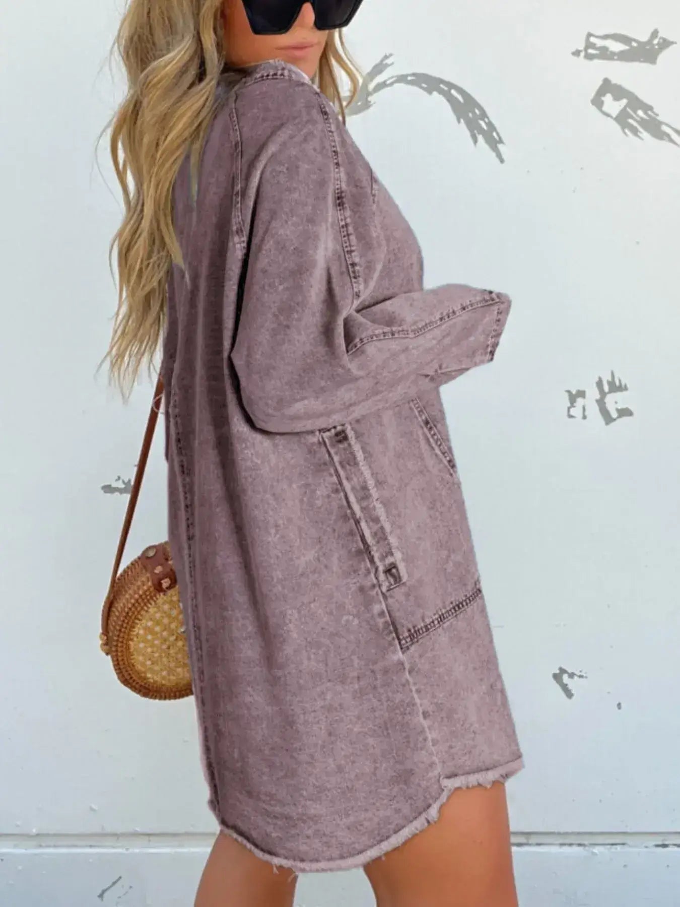 Model showcasing a relaxed oversized button-front denim shirt dress with pockets against a textured background.