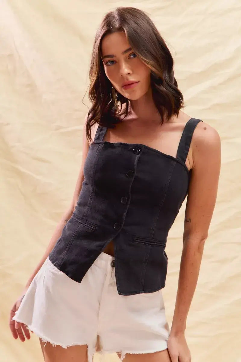 Model wearing a black button-down sleeveless denim top paired with white shorts against a neutral background.