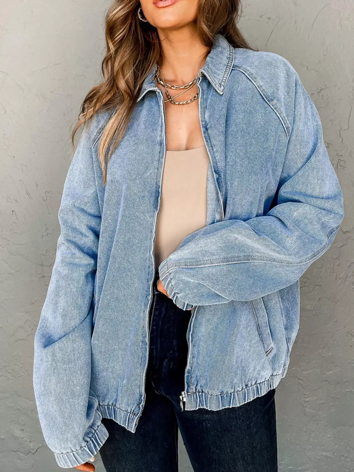 Woman in blue denim jacket with elastic edge, zip up closure, and relaxed fit, styled for a casual look.