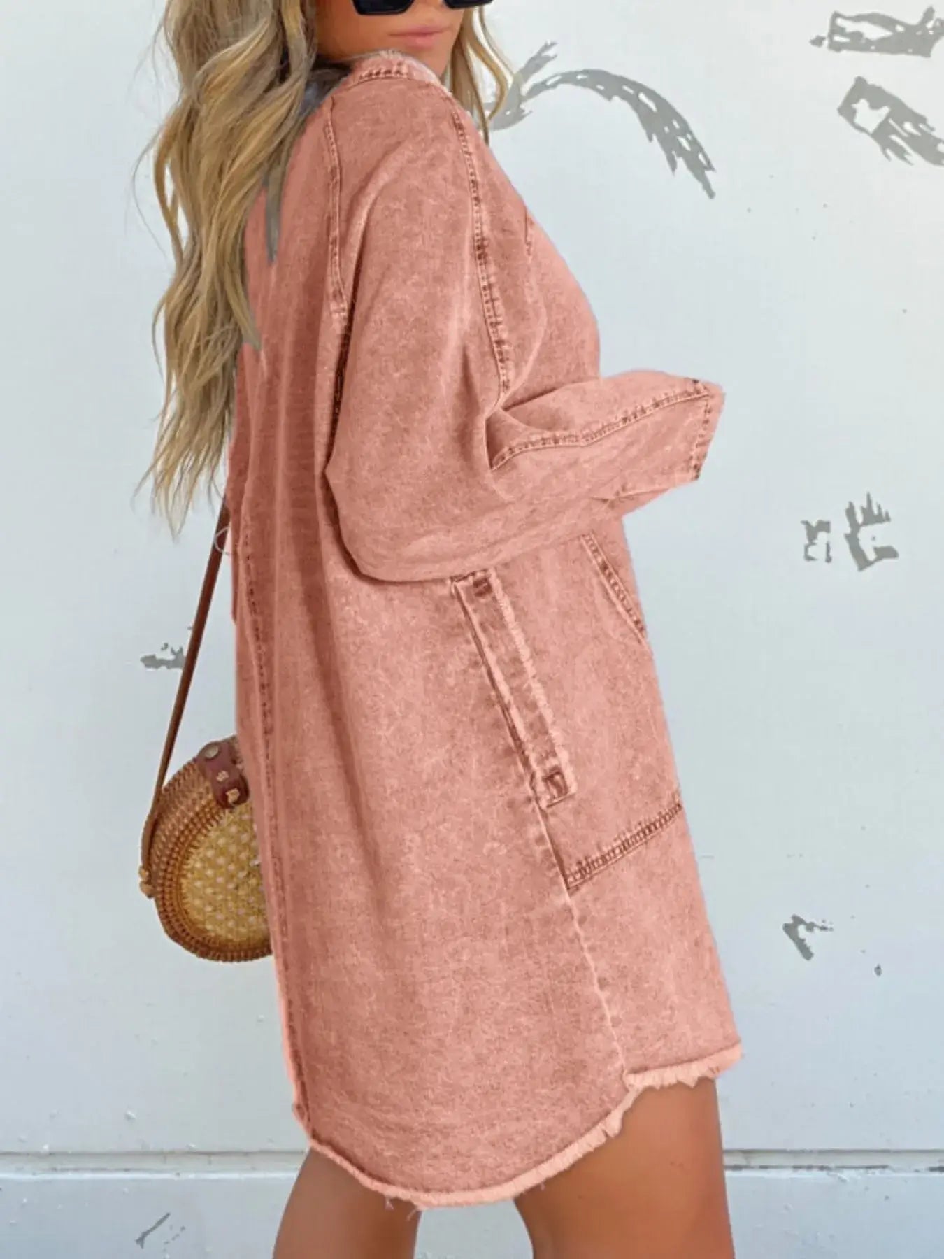 Model wearing a relaxed pink denim shirt dress with pockets and a fashionable round handbag.
