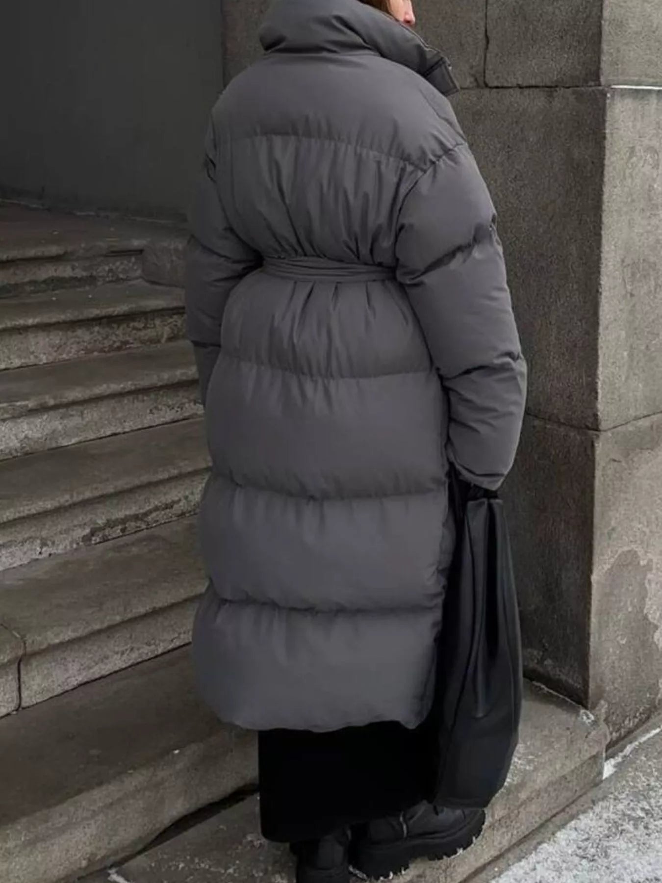 Longline Padded Winter Coat Belted worn by a woman, featuring a cozy gray design on outdoor stairs.