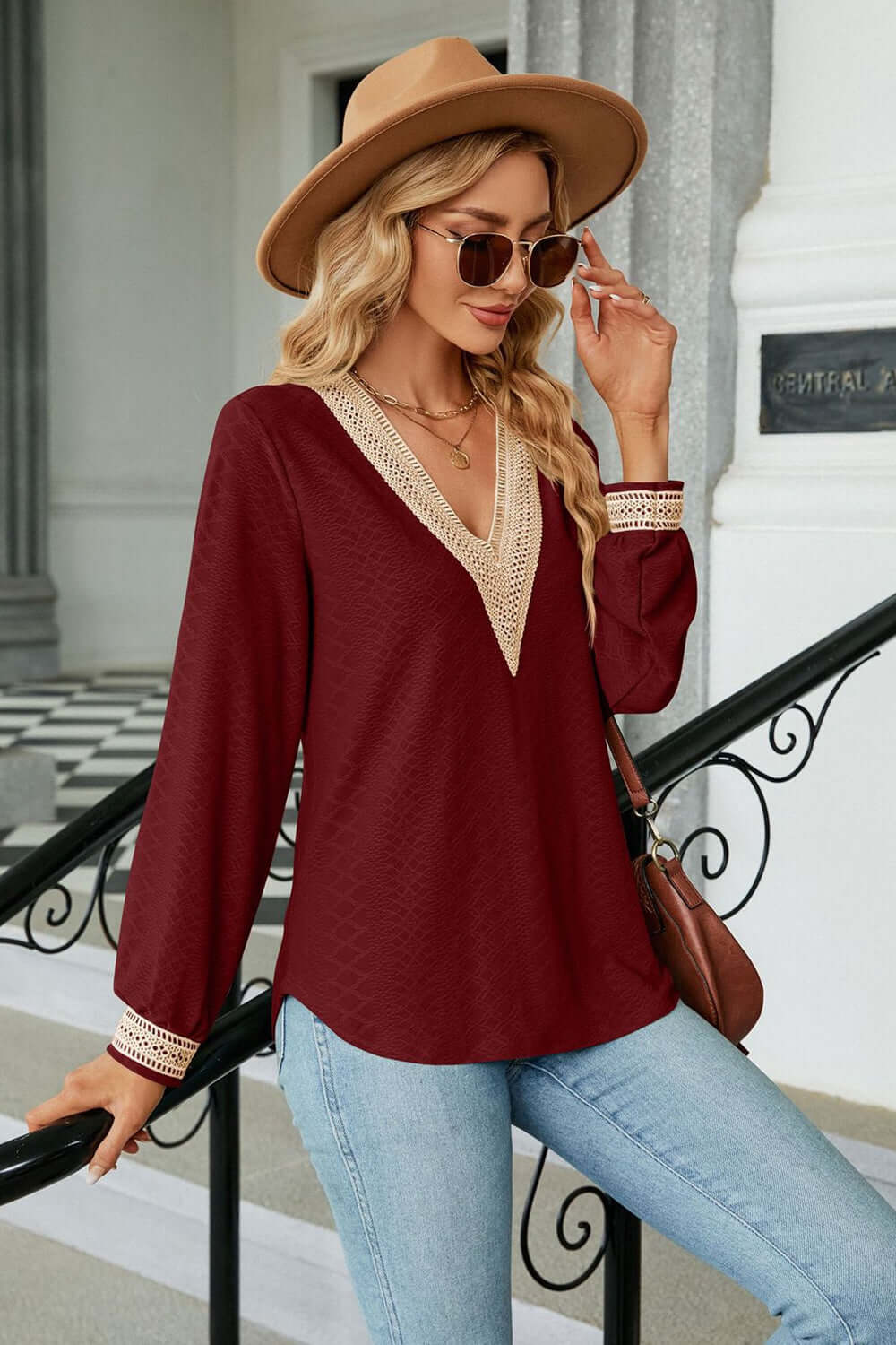 Model wearing V-Neck Long Sleeve Blouse in burgundy, styled with jeans, hat, and sunglasses for a casual yet elegant look.