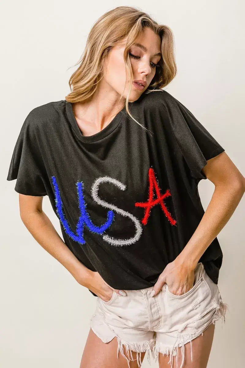 BiBi Metallic Letter Short Dolman Sleeve Top featuring oversized fit and rhinestone details, styled with casual shorts.
