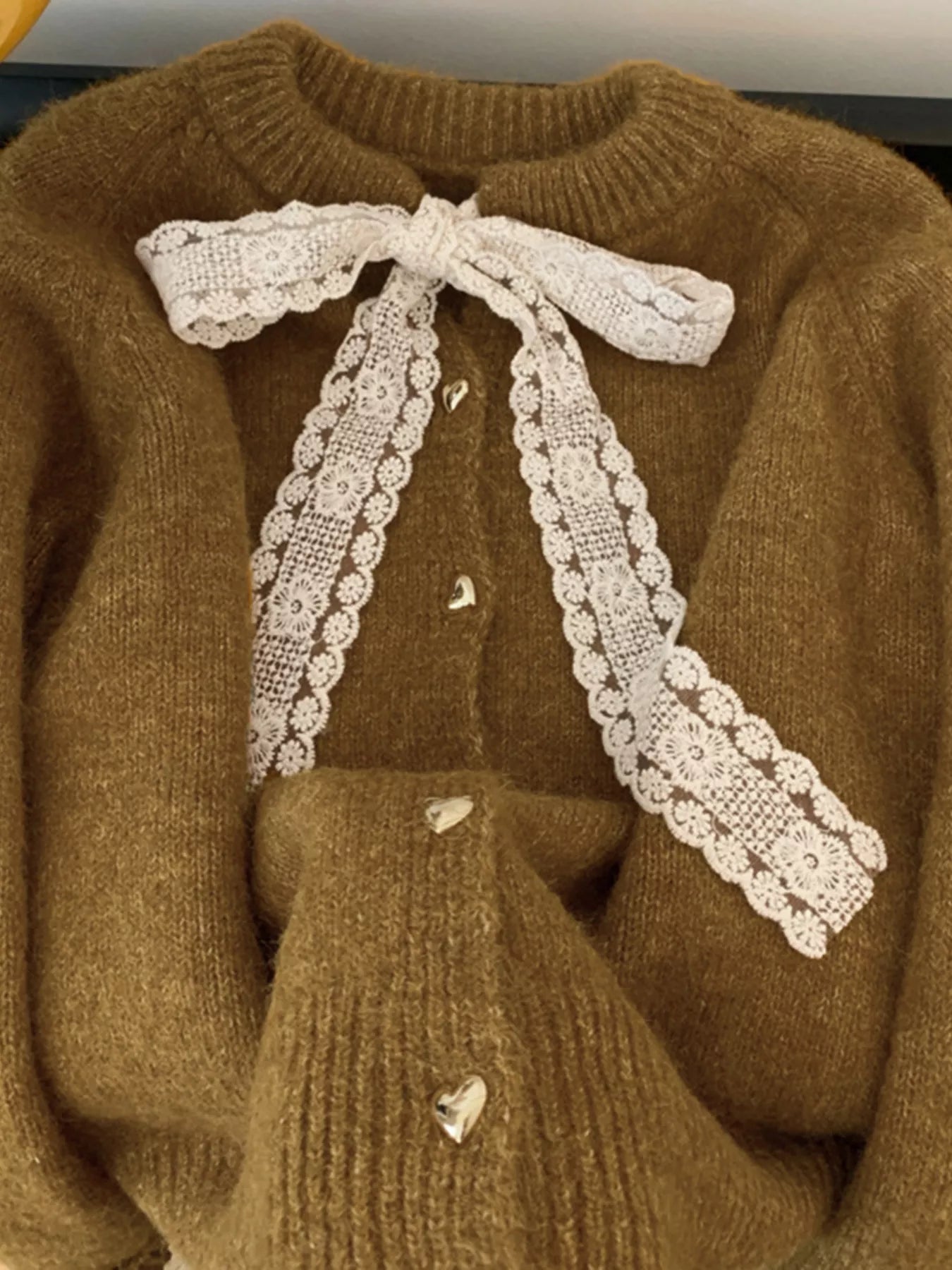 Lace Bowknot Knit Cardigan featuring a lace bow and heart buttons on a soft brown background.