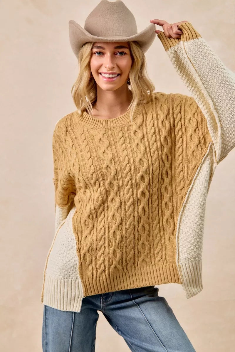 Model wearing BiBi Cable Knit Hacci Combo Sweater with uneven hem and cowboy hat, showcasing cozy fashion.