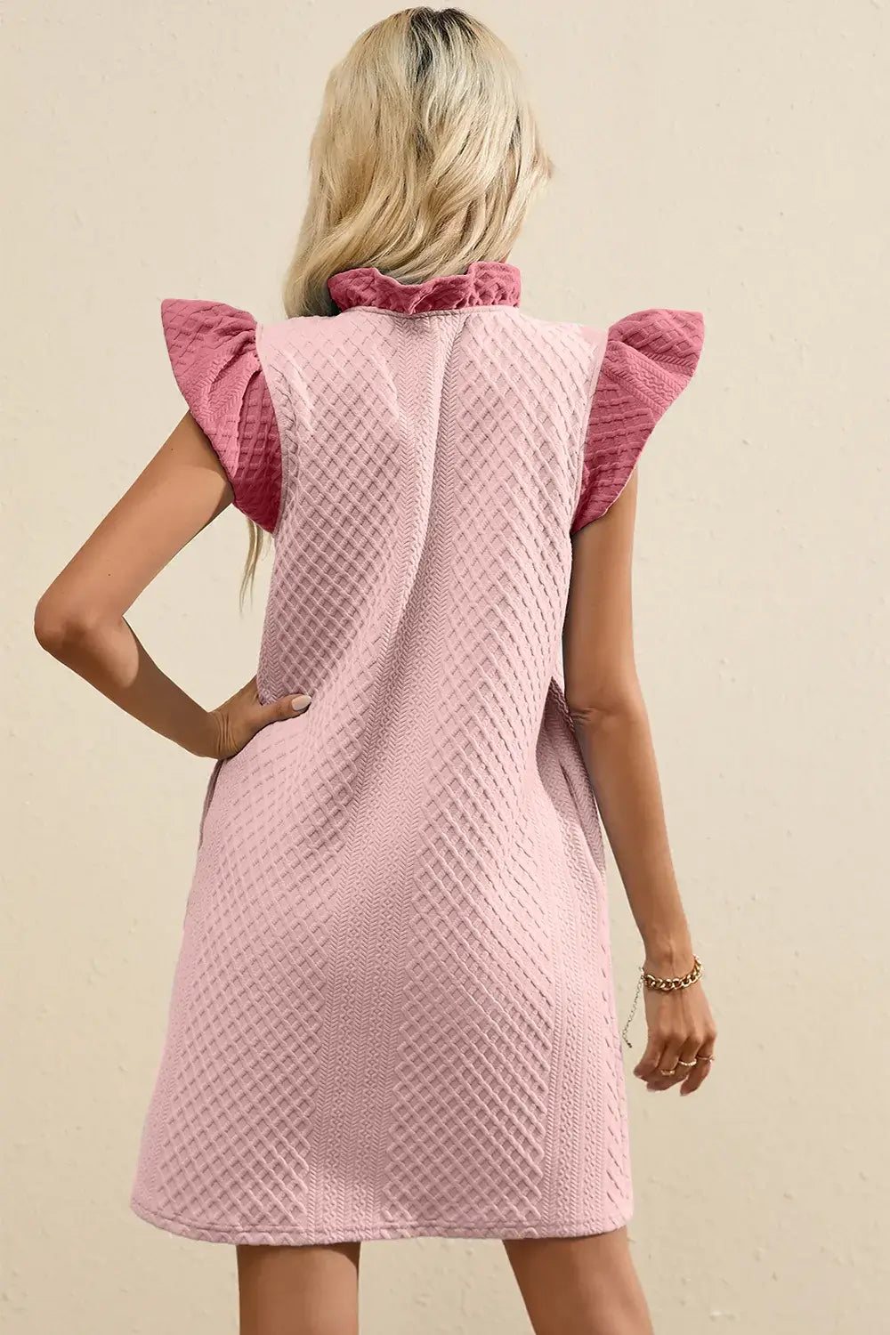 Back view of a ruffled V-neck cap sleeve mini dress in pink with textured fabric for a feminine everyday look.