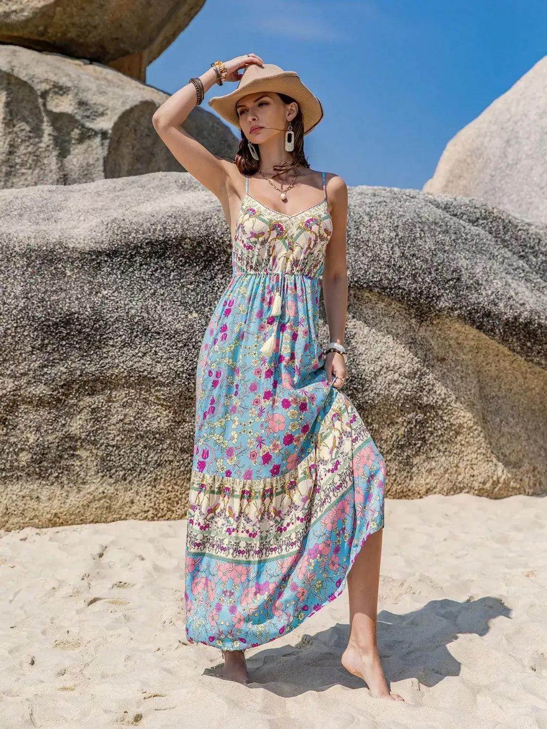 Model wearing a Tassel Floral Print Cami Dress on the beach with a straw hat and bohemian accessories.