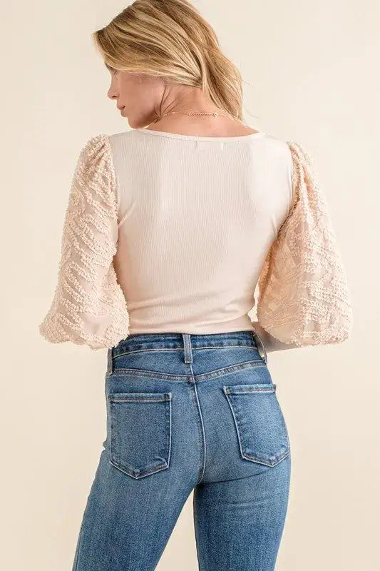 Back view of the textured puff sleeve bodysuit with lace sleeves paired with high-waisted jeans.