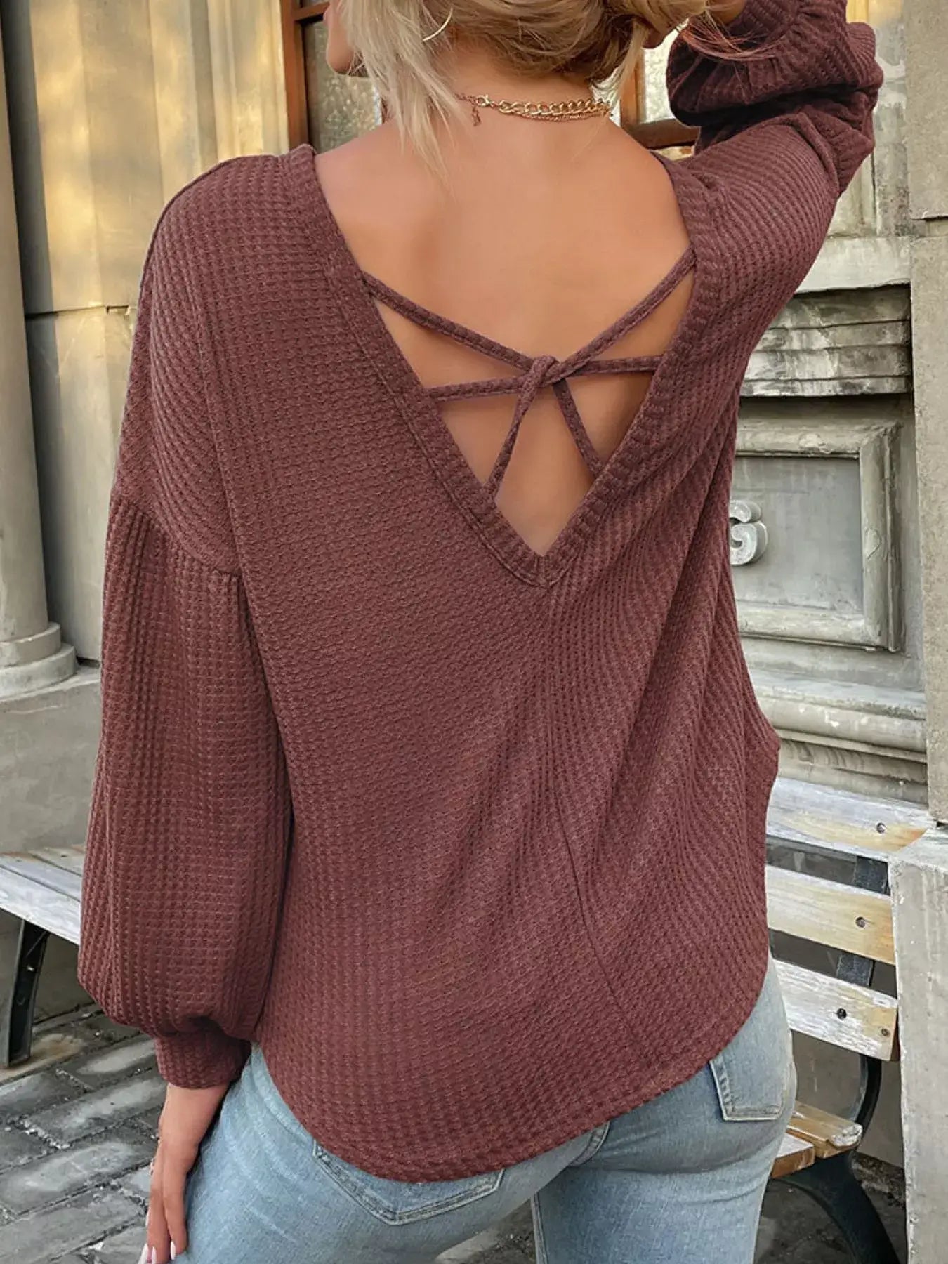 Back view of a woman wearing a burgundy waffle knit round neck top with long sleeves and stylish crisscross detailing.