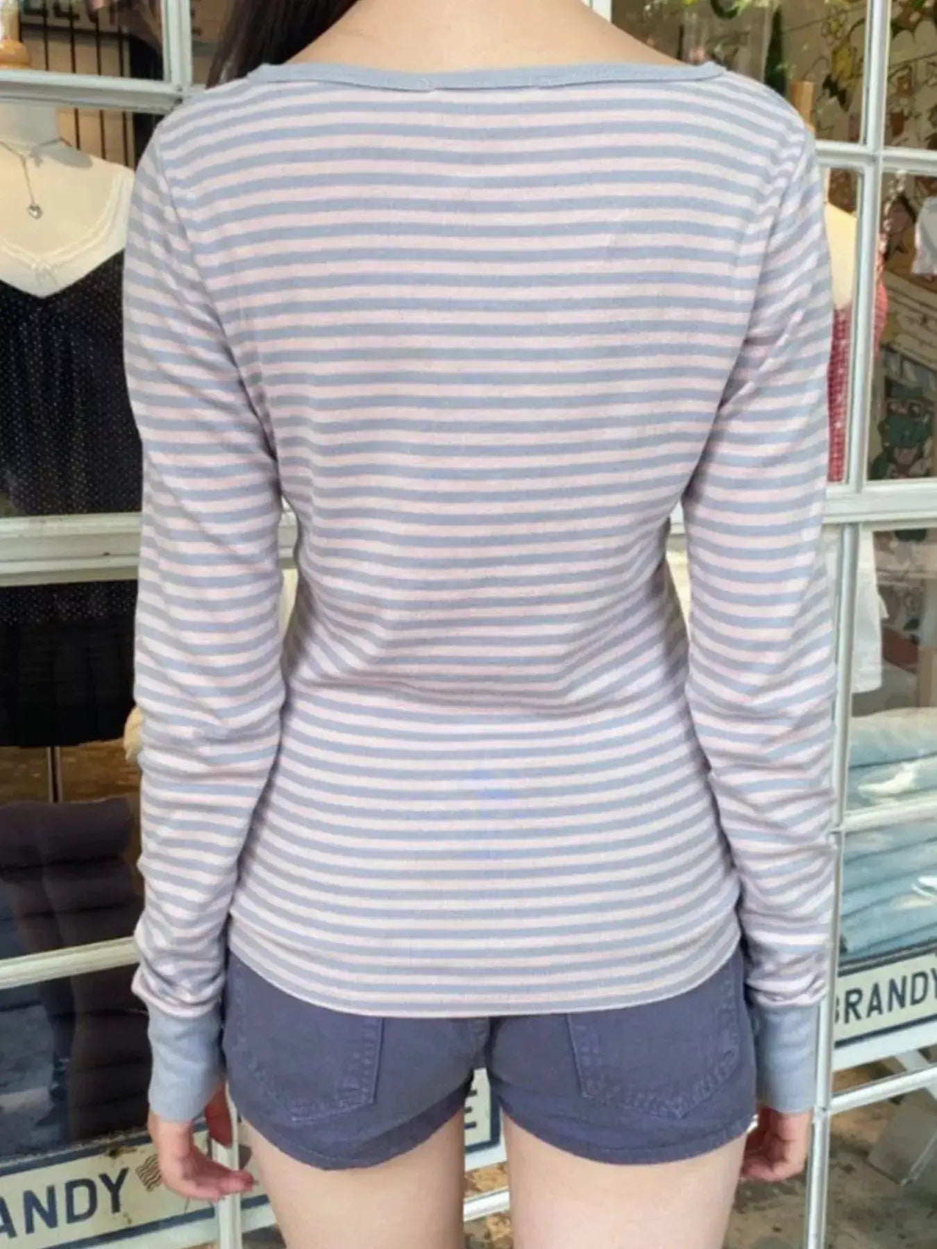 Back view of a woman wearing a striped long sleeve Henley t-shirt paired with shorts.