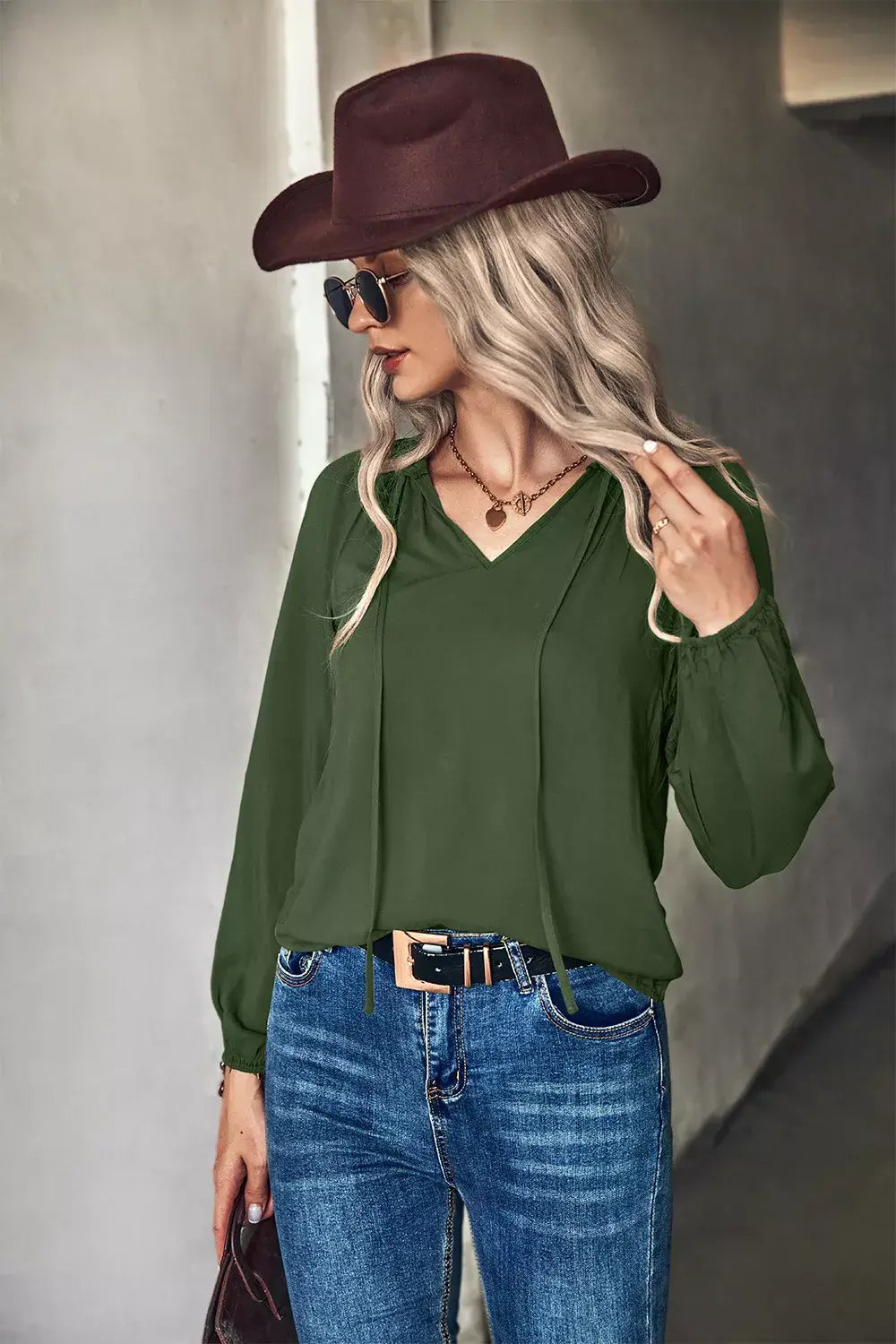 Tie neck long sleeve blouse in green worn with denim, featuring a stylish hat and sunglasses for chic office wear.