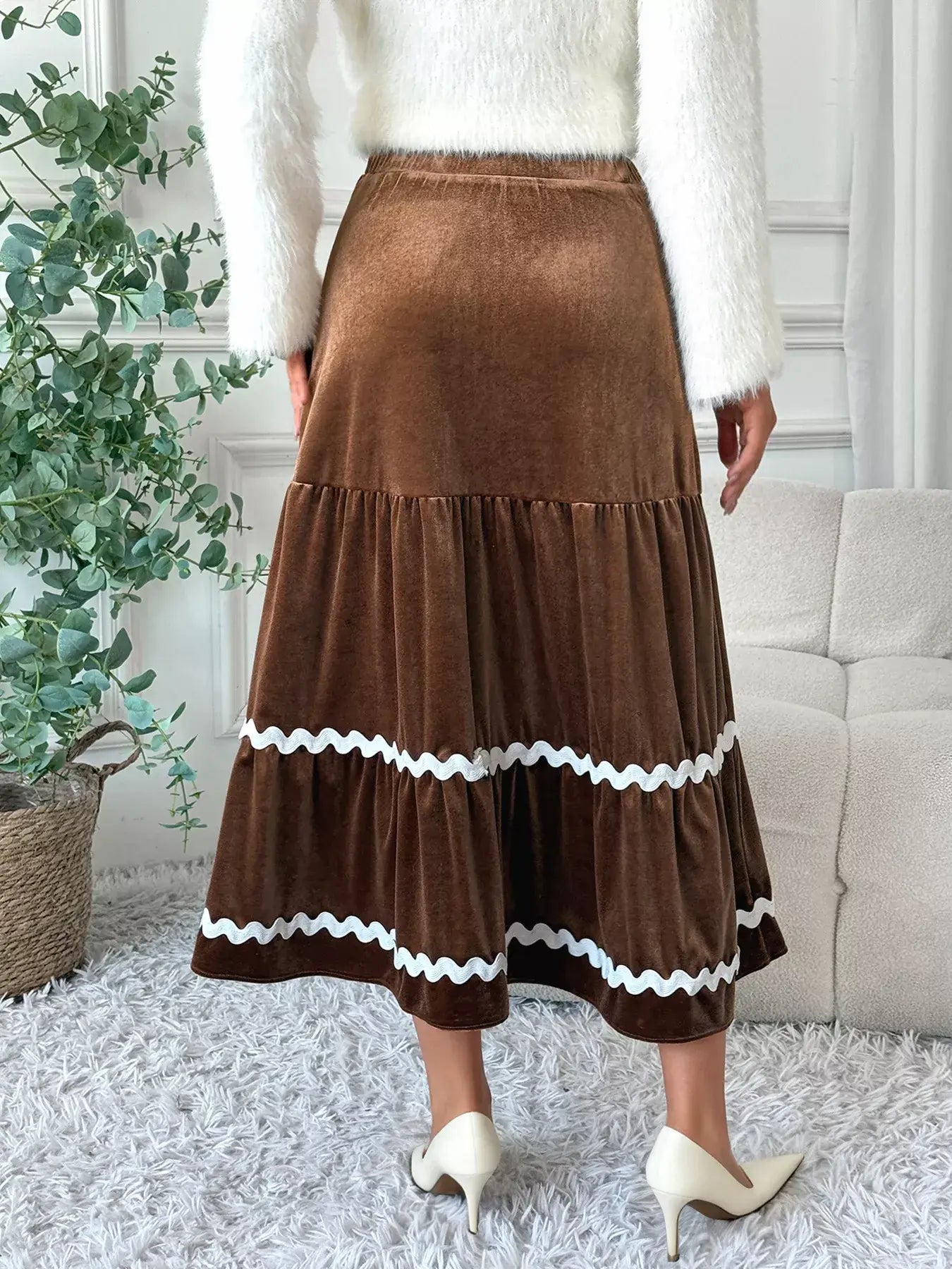 Back view of a woman wearing a Velvet Tiered Midi Skirt in brown with tiered design and white detailing.