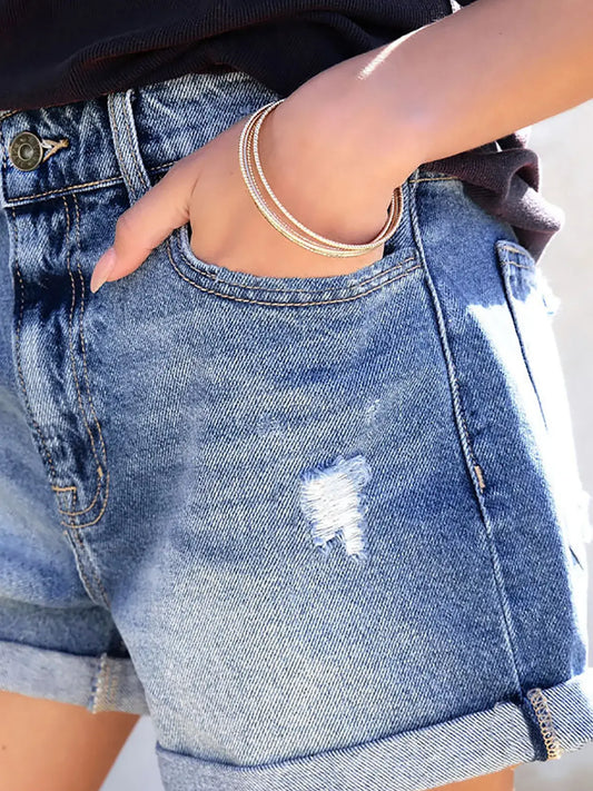 Close-up of distressed denim shorts for women with rolled cuffs and a hand in the pocket, showcasing style and comfort.
