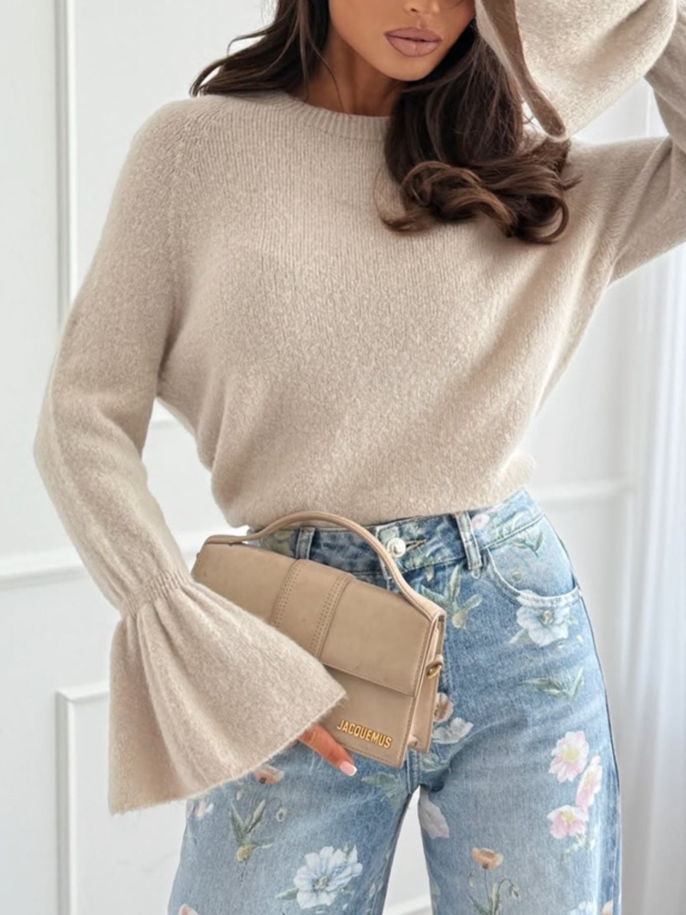Model wearing a Round Neck Flounce Sleeve Sweater in beige with floral jeans and a stylish bag.
