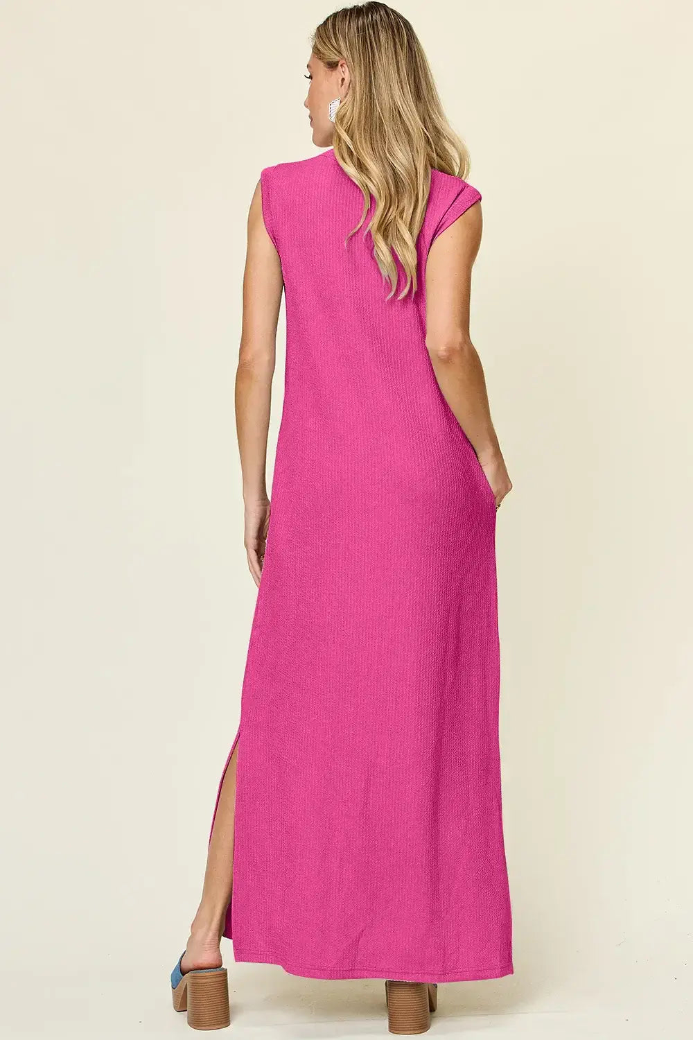 Back view of a woman wearing a pink sleeveless maxi dress with a mock neck and side slit for casual wear.