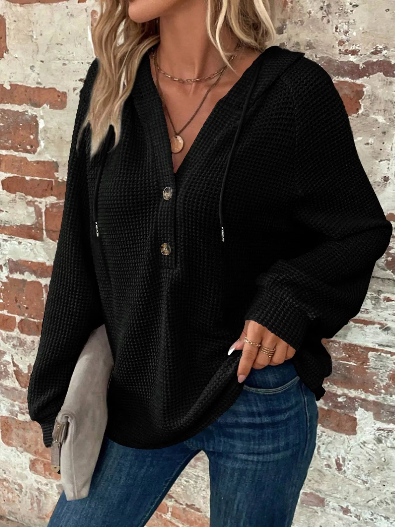 Full Size Button Detail Waffle Knit Hoodie Plus Size in black worn with denim against a textured brick wall.