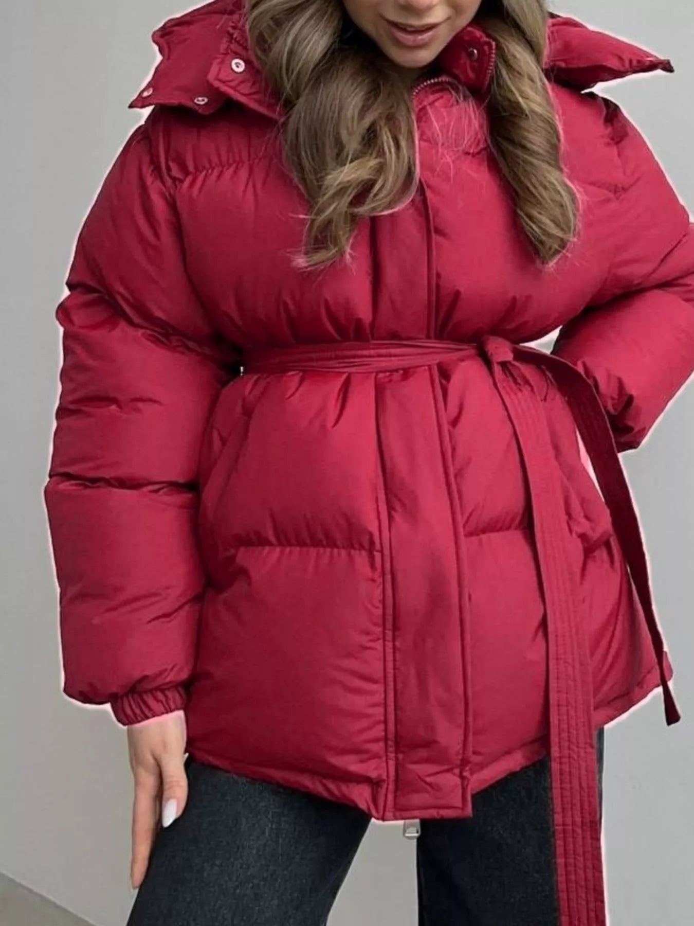 Mid Length Hooded Winter Coat Belted in red on a model, featuring a belted waist, pockets, and thick lining.