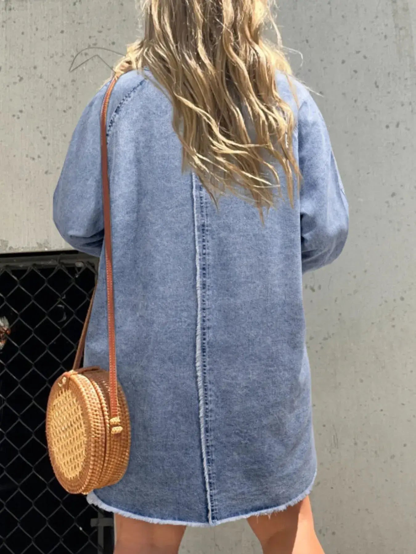 Back view of a woman in a denim shirt dress with a round straw bag on a sunny day, showcasing a relaxed fit.