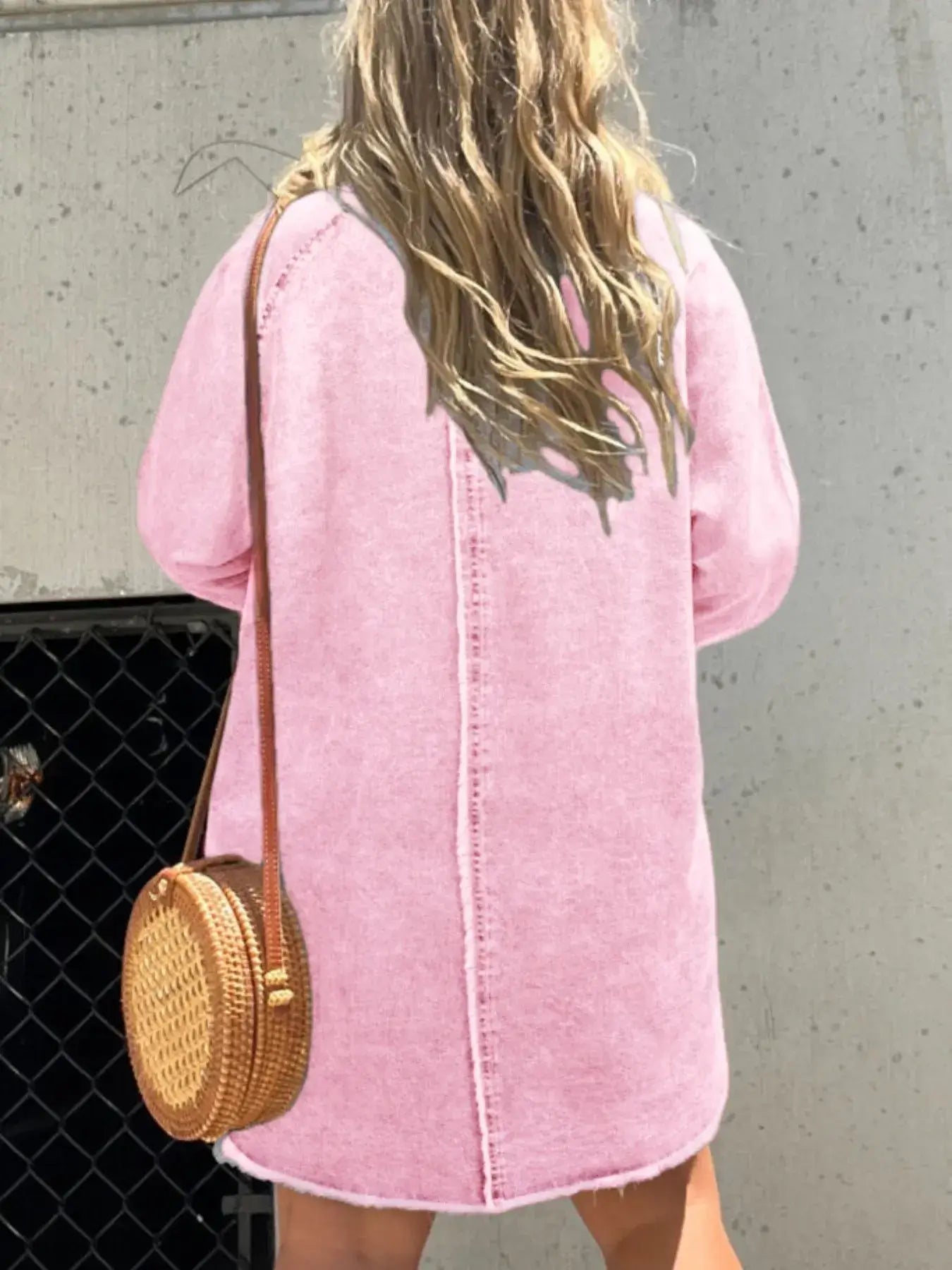 Back view of a woman wearing a pink oversized denim dress with a round handbag.