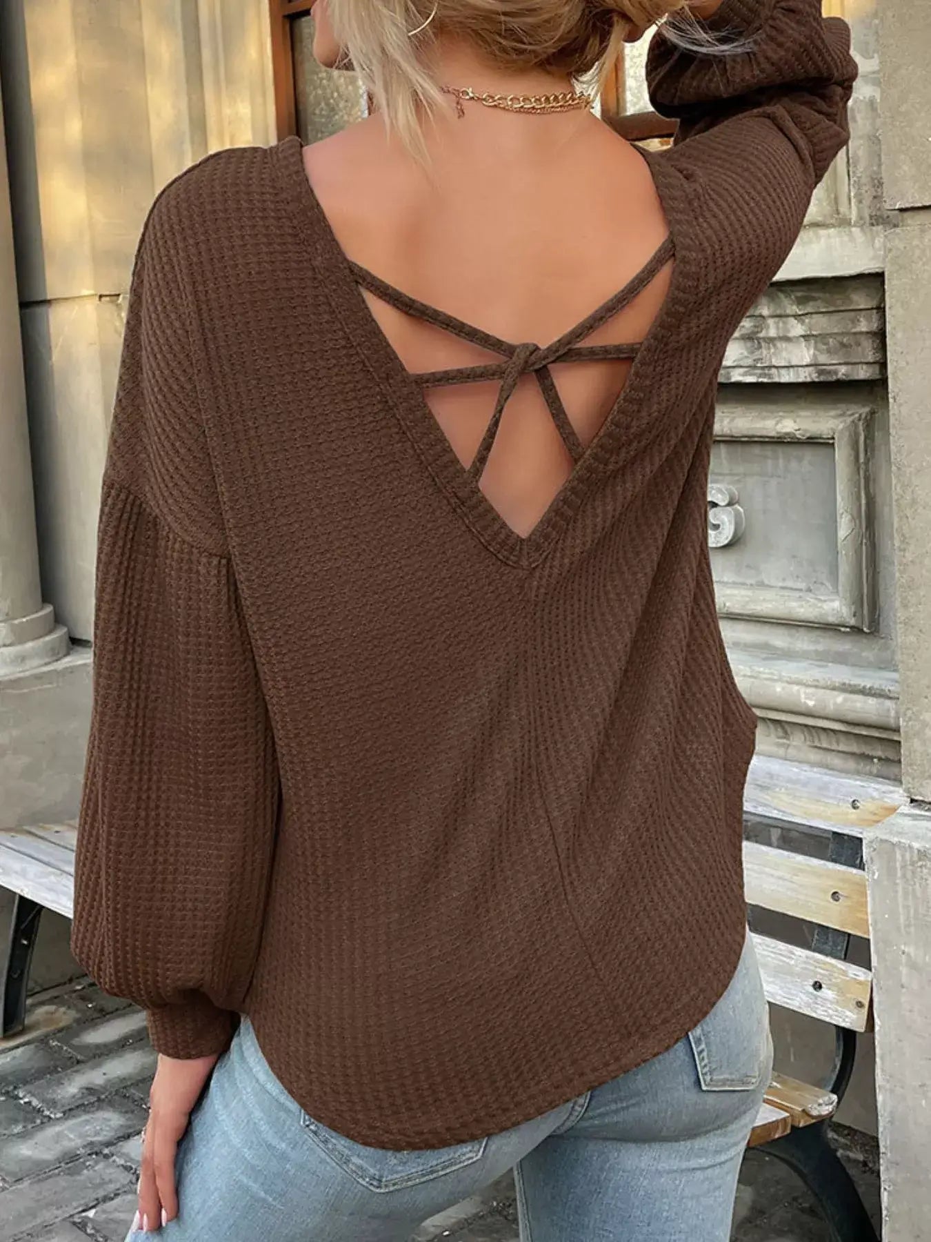 Back view of a woman wearing a brown waffle knit top with a crisscross design, styled with light blue jeans.