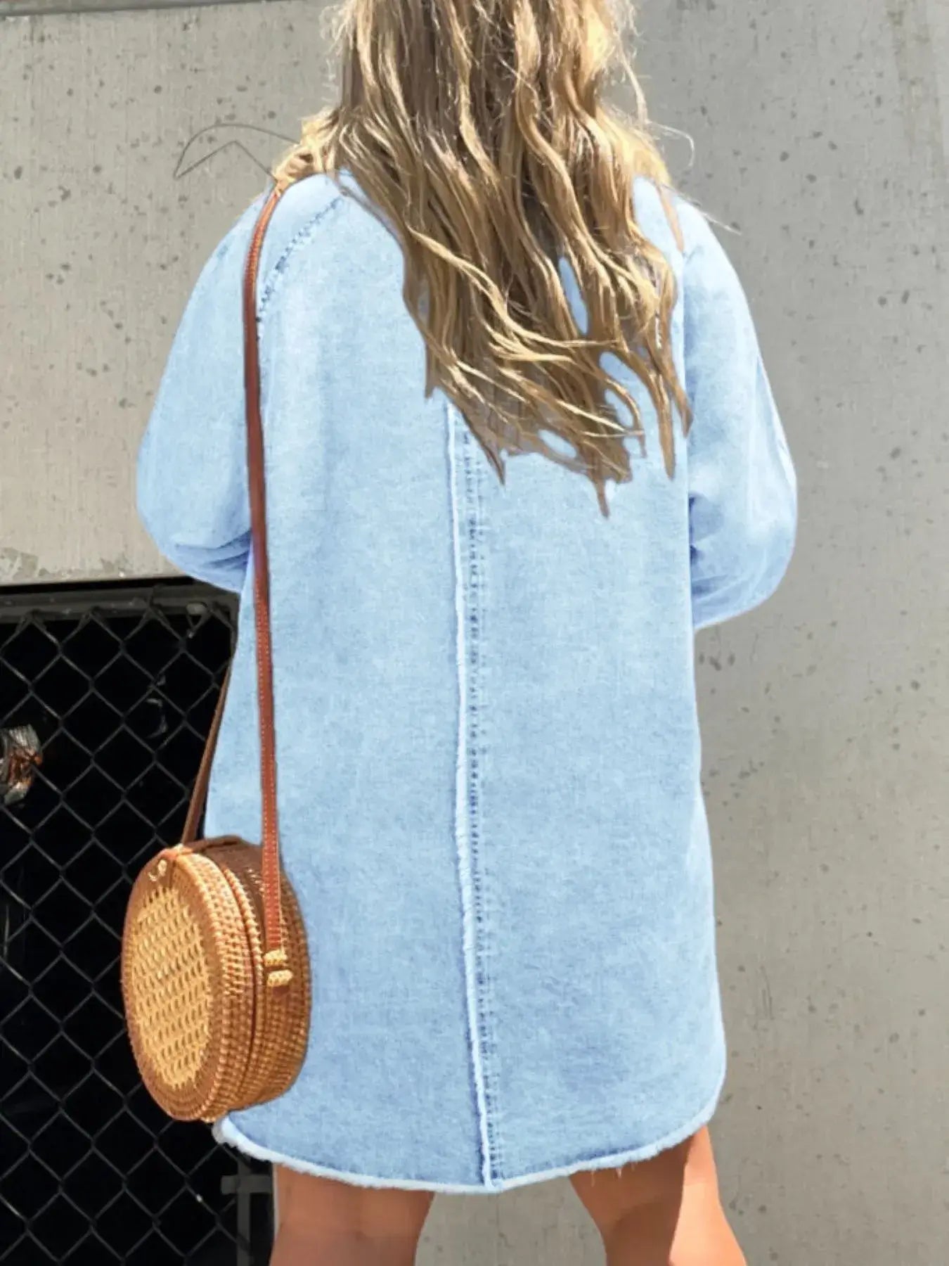 Woman wearing a light blue button-front denim shirt dress, showcasing a relaxed fit and styled with a round woven bag.