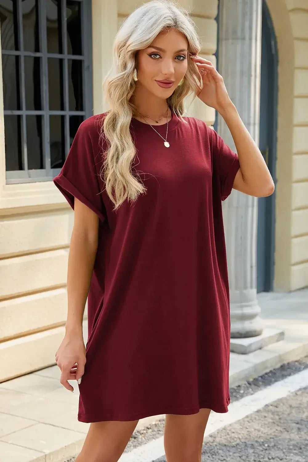 Woman wearing a burgundy round neck rolled short sleeve tee dress, styled casually outdoors.