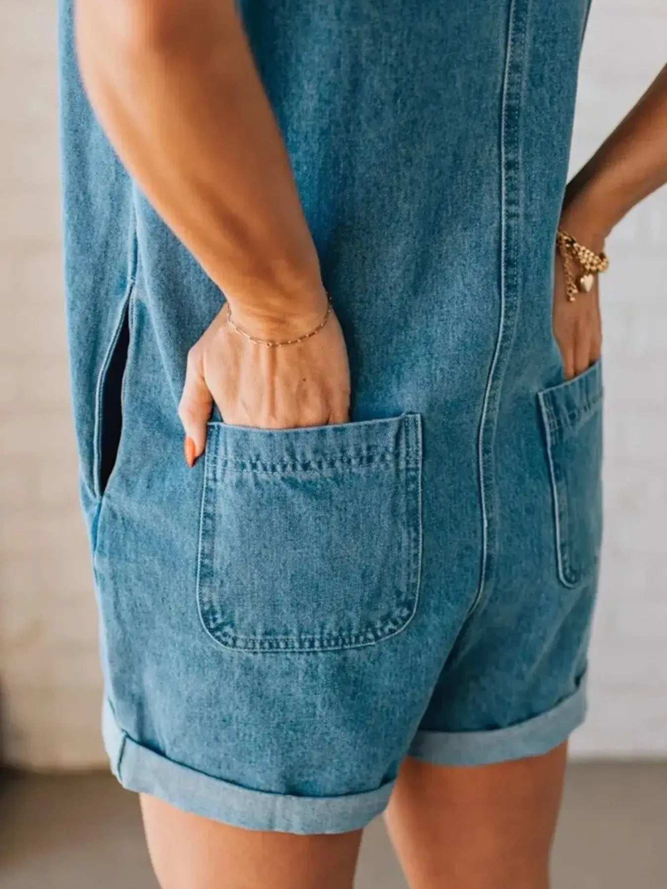 Detail view of a woman wearing a zip front sleeveless denim romper, showcasing functional pockets and rolled hems.