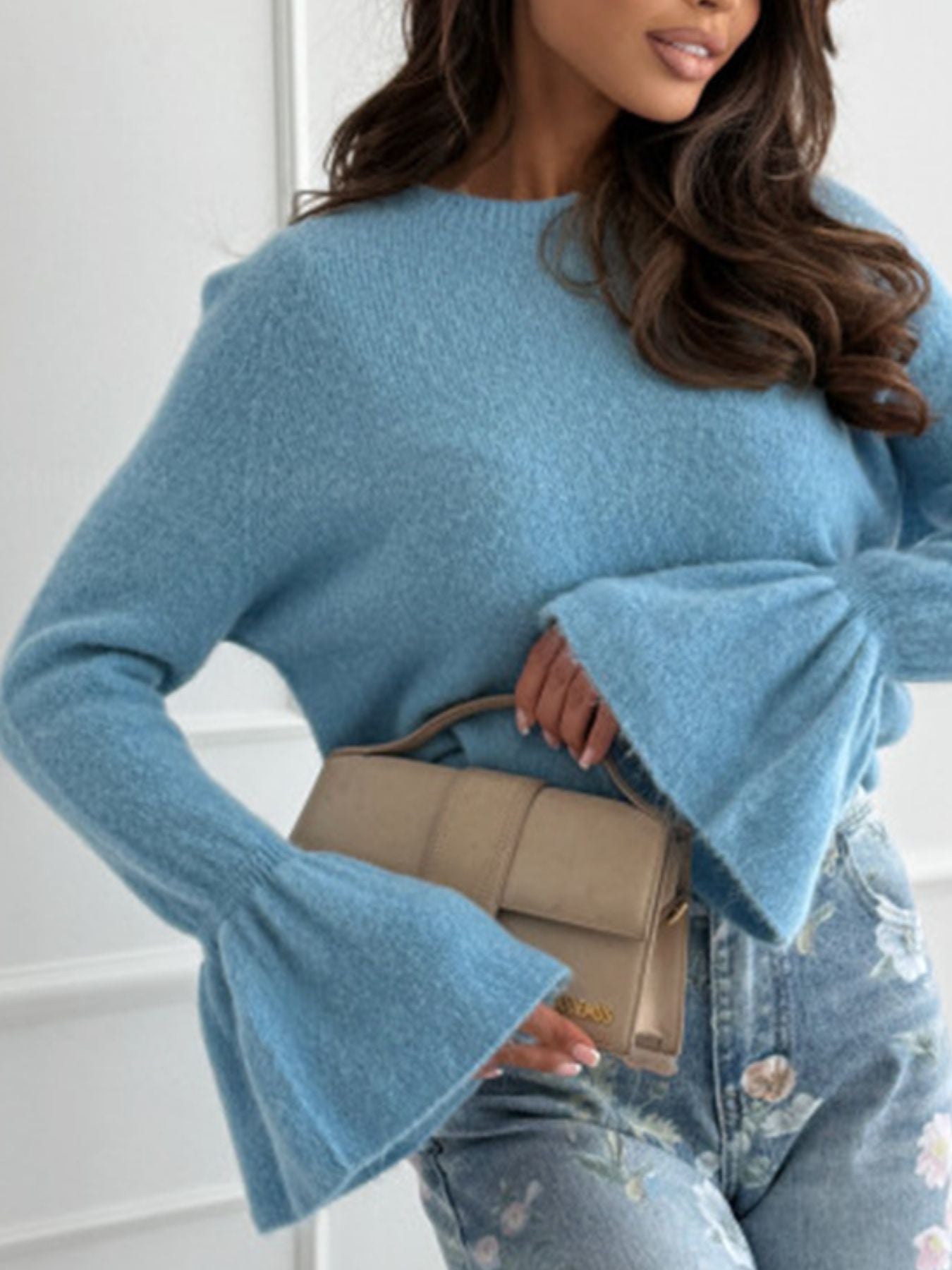 Model wearing a Round Neck Flounce Sleeve Sweater in blue, paired with a stylish handbag and floral jeans.