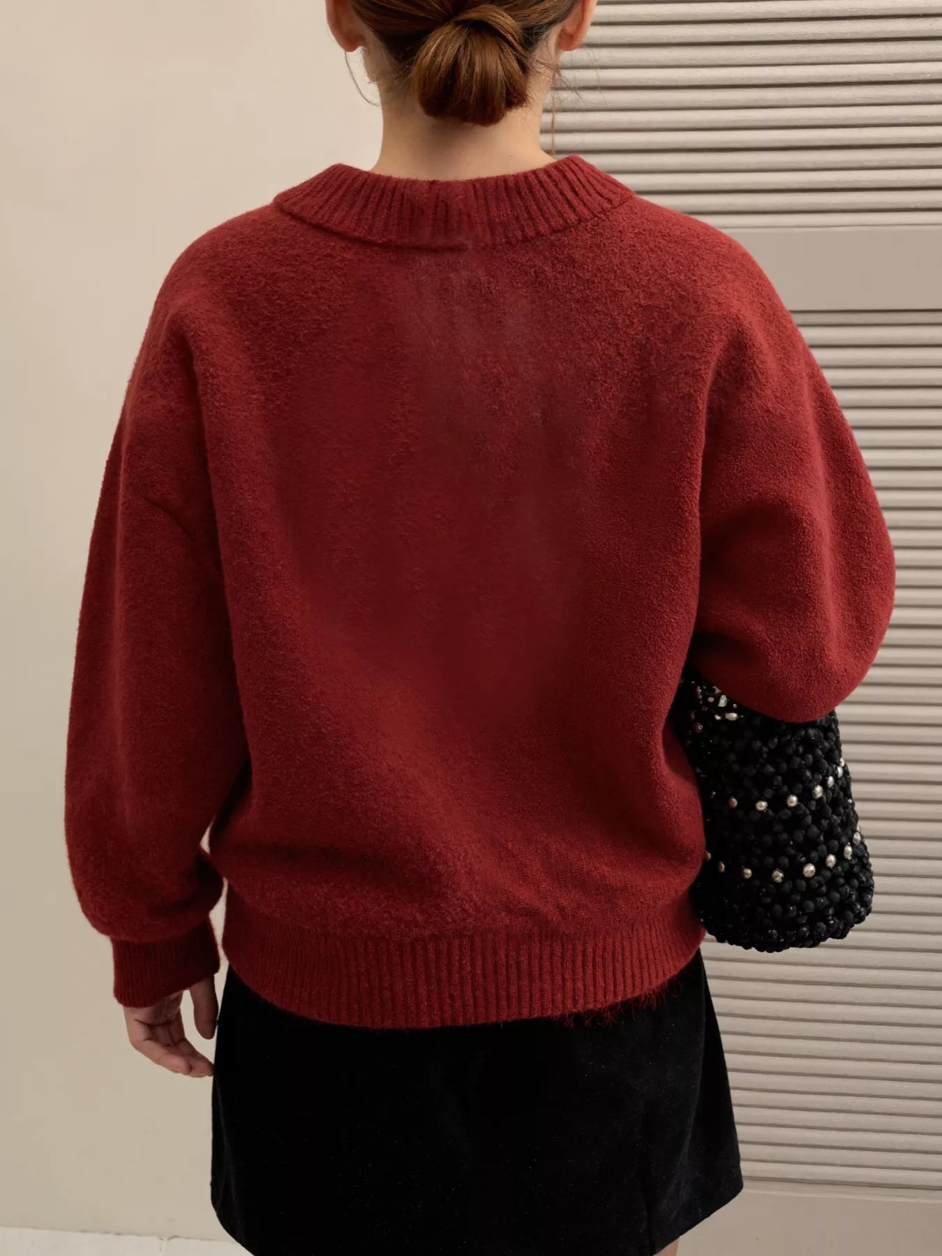 Back view of a woman wearing a cozy red Lace Bowknot Knit Cardigan, holding a black beaded handbag.