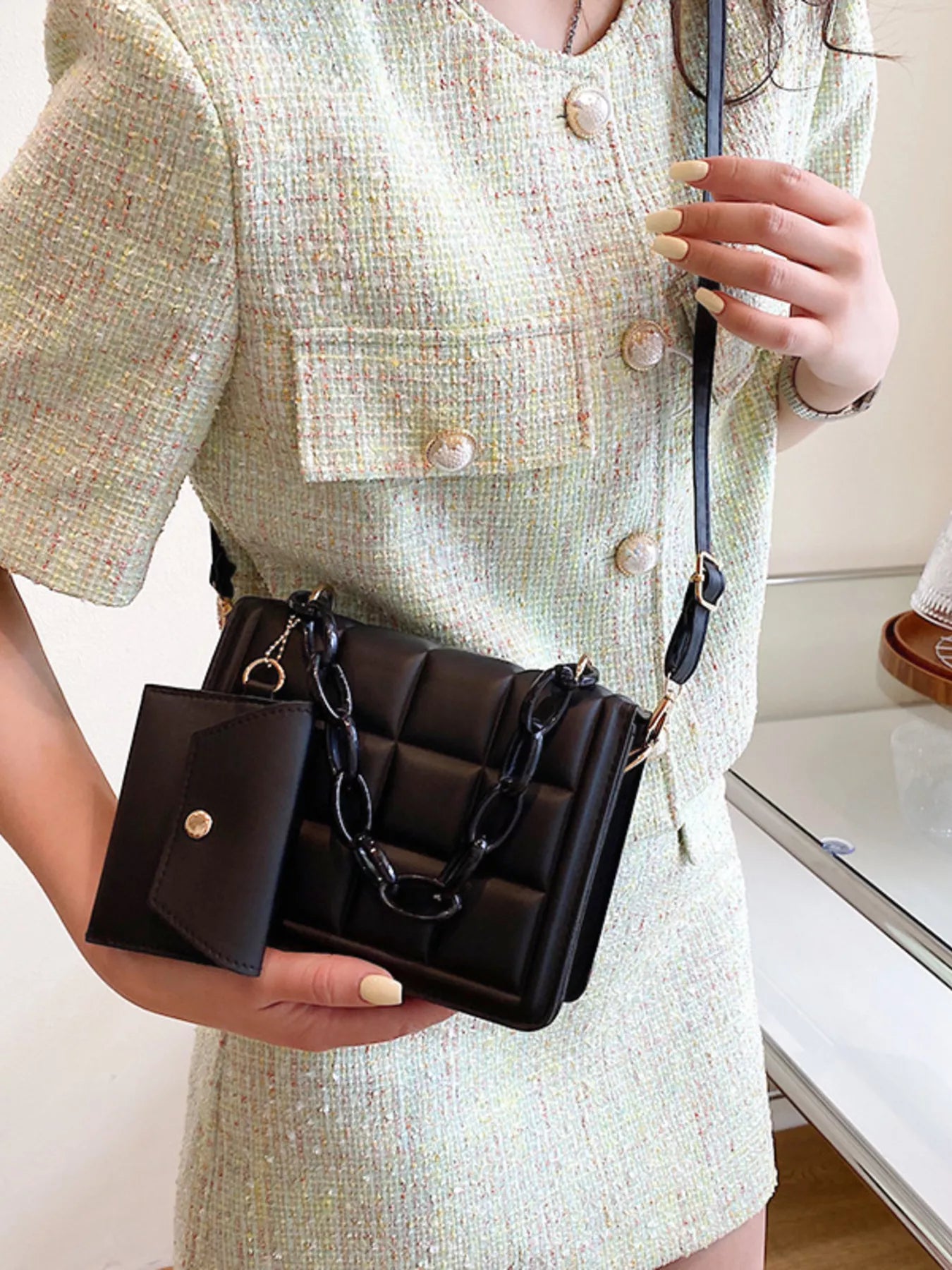 Model holding a Quilted Chain Strap Crossbody Bag in black PU leather, styled with a light-colored outfit.