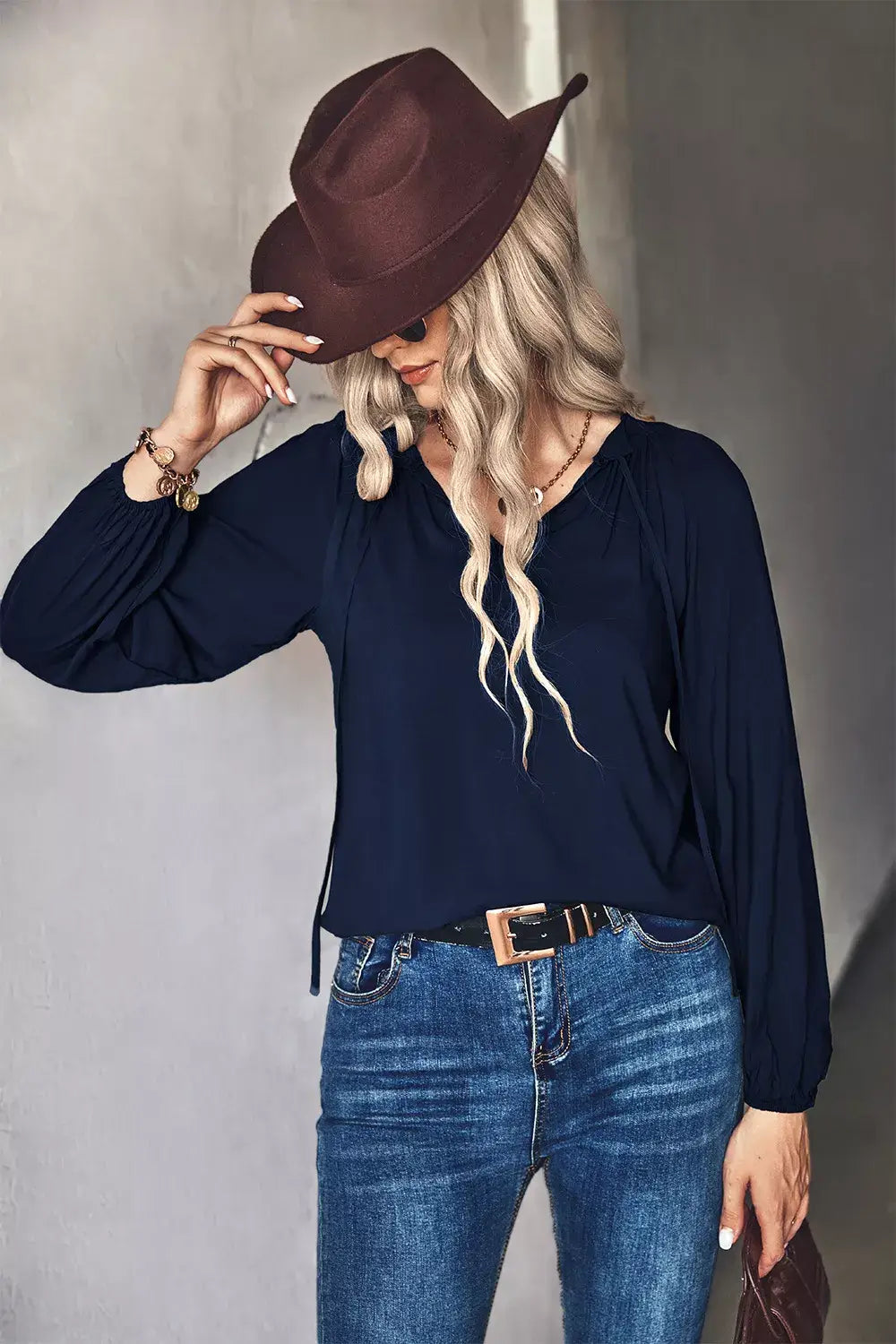 Model wearing a tie neck long sleeve blouse with long sleeves and a hat, styled with jeans for a chic look.
