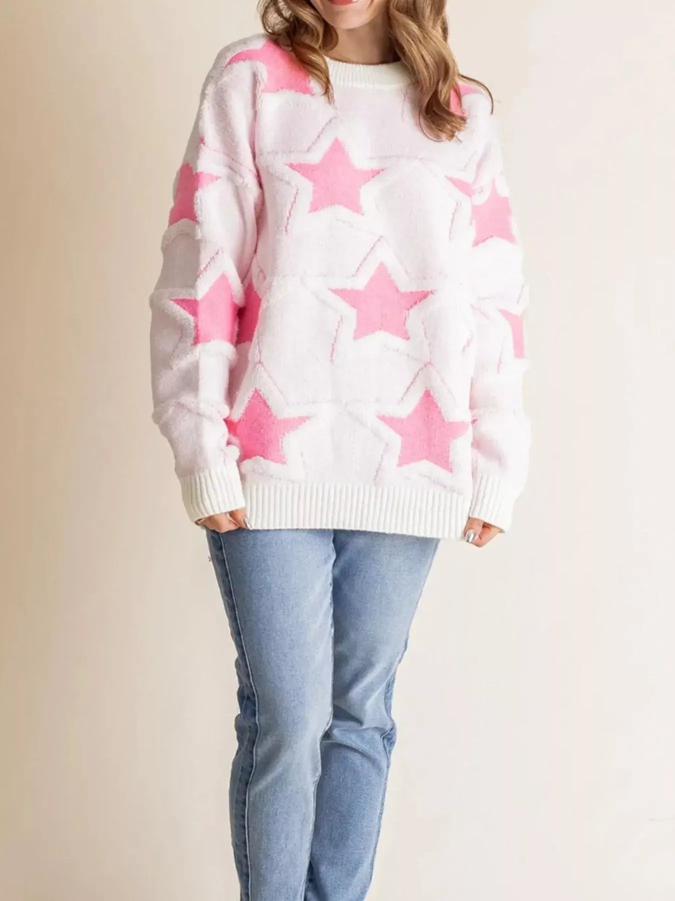 Oversized star pattern ribbed edge drop shoulder sweater worn with blue jeans, featuring a playful star design in pink and white.
