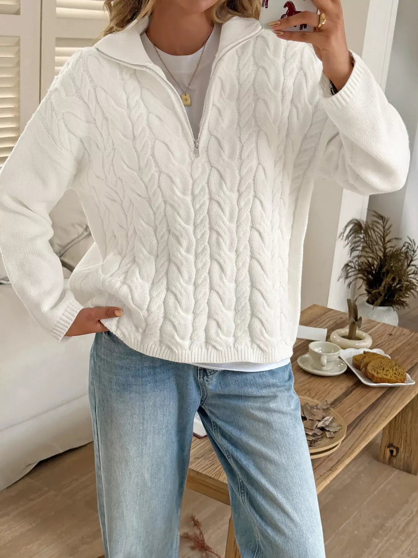Model wearing a zip collar cable-knit sweater in white, showcasing the chunky knit design and zip-up collar.
