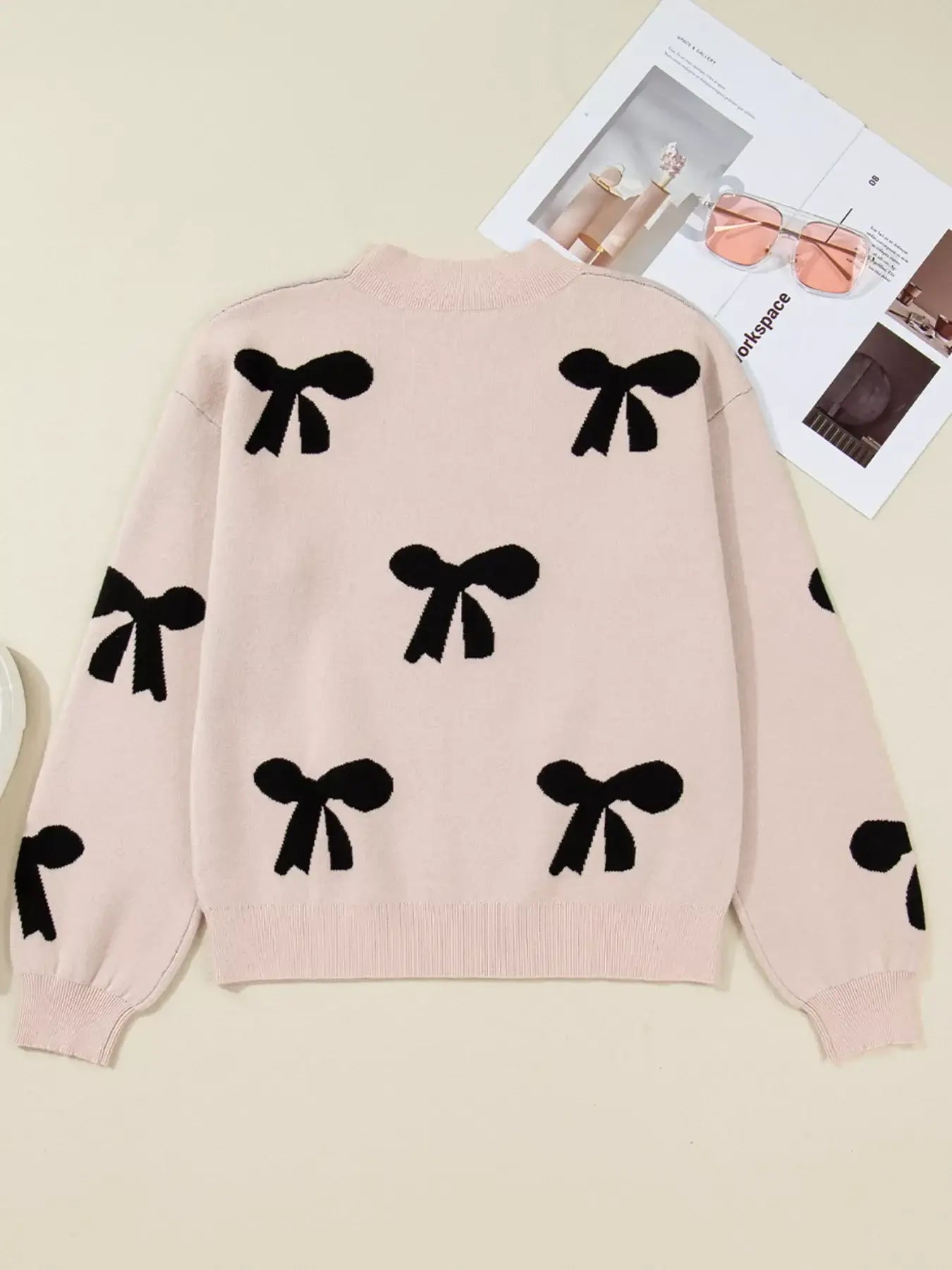 Pearl embellished bow pattern loose sweater, featuring black bows on a soft pink knit, showcasing elegance and comfort.