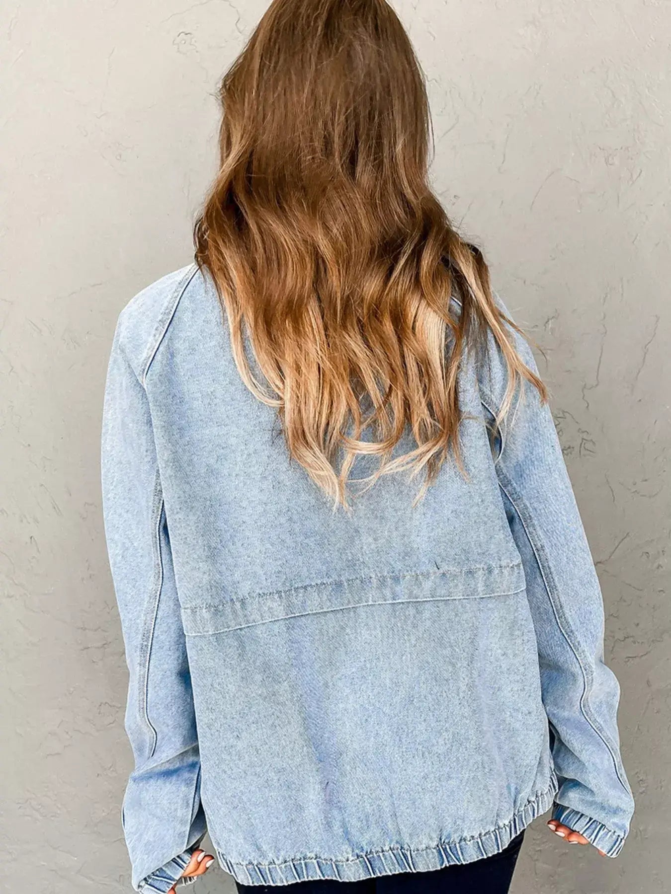 Back view of a woman wearing a light blue elastic edge denim jacket with long sleeves.