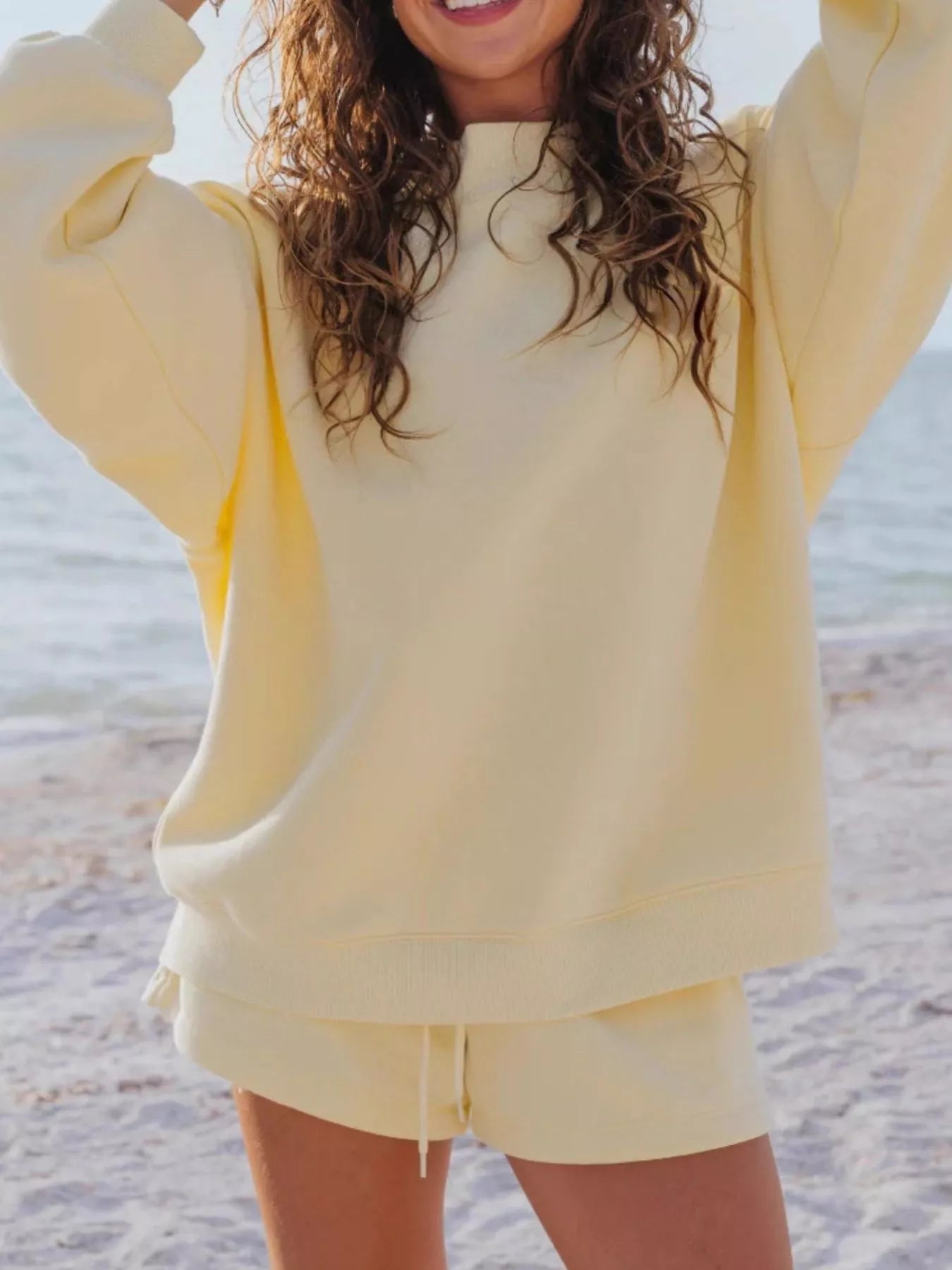 Relaxed Fit Round Neck Sweatshirt and Shorts Set in yellow worn by a smiling woman at the beach.