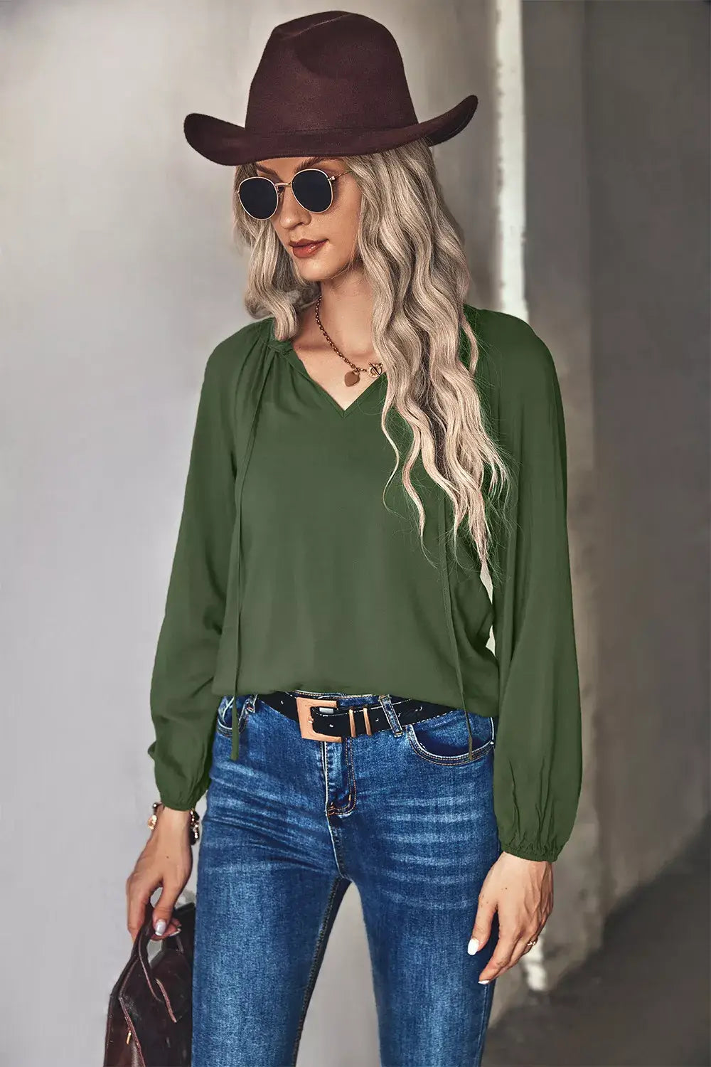 Tie neck long sleeve blouse in green worn with denim and hat, styled for an elegant casual look.
