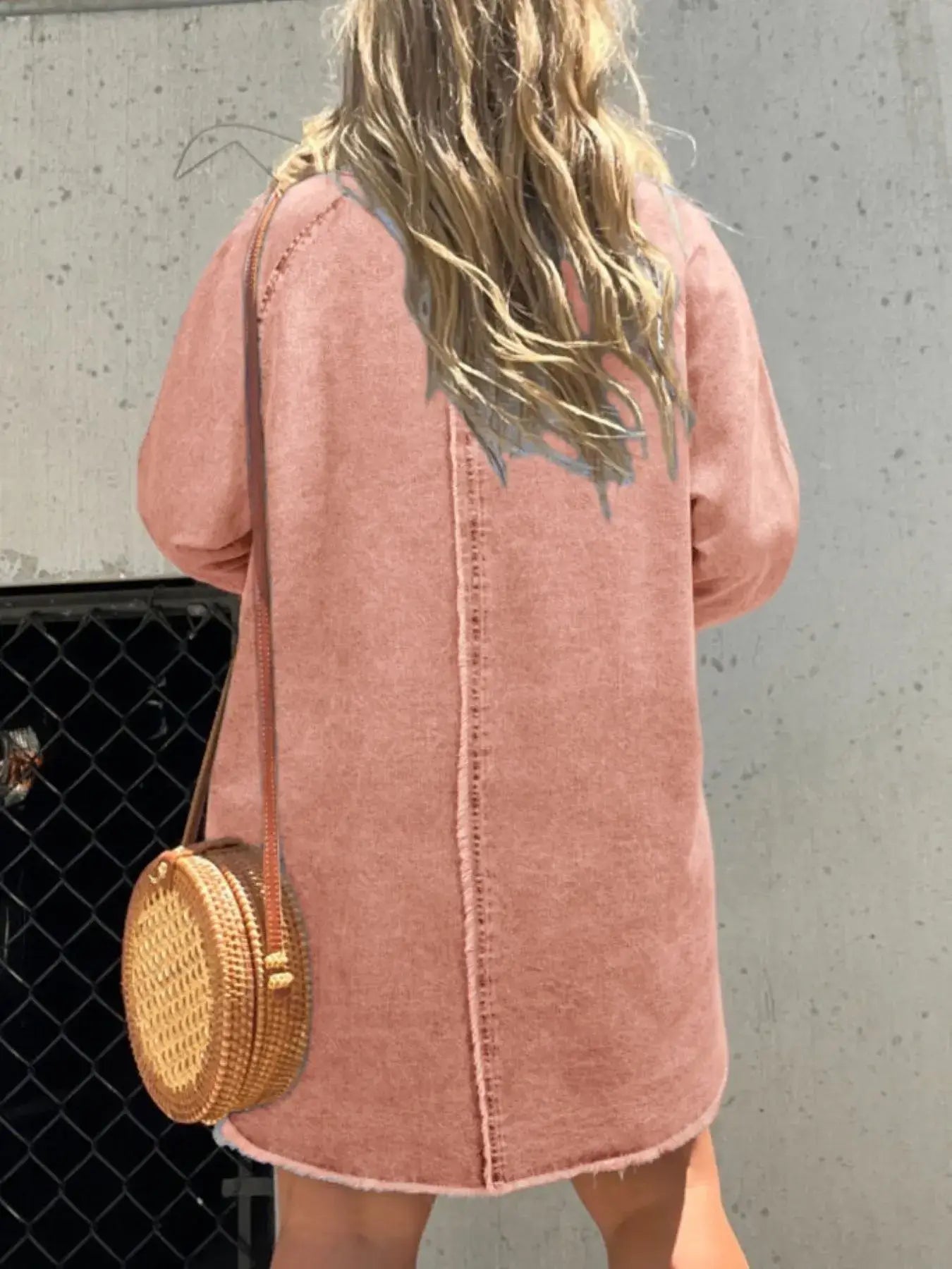 Back view of a woman wearing a pink oversized denim shirt dress with a round woven bag.